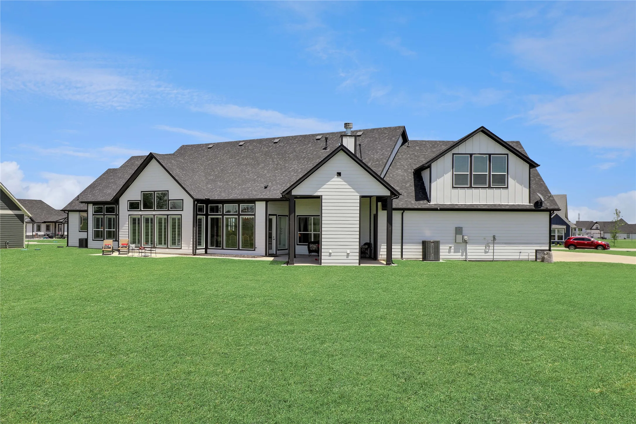 Rear view of house featuring board and batten siding, a lawn, a patio, and roof with shingles