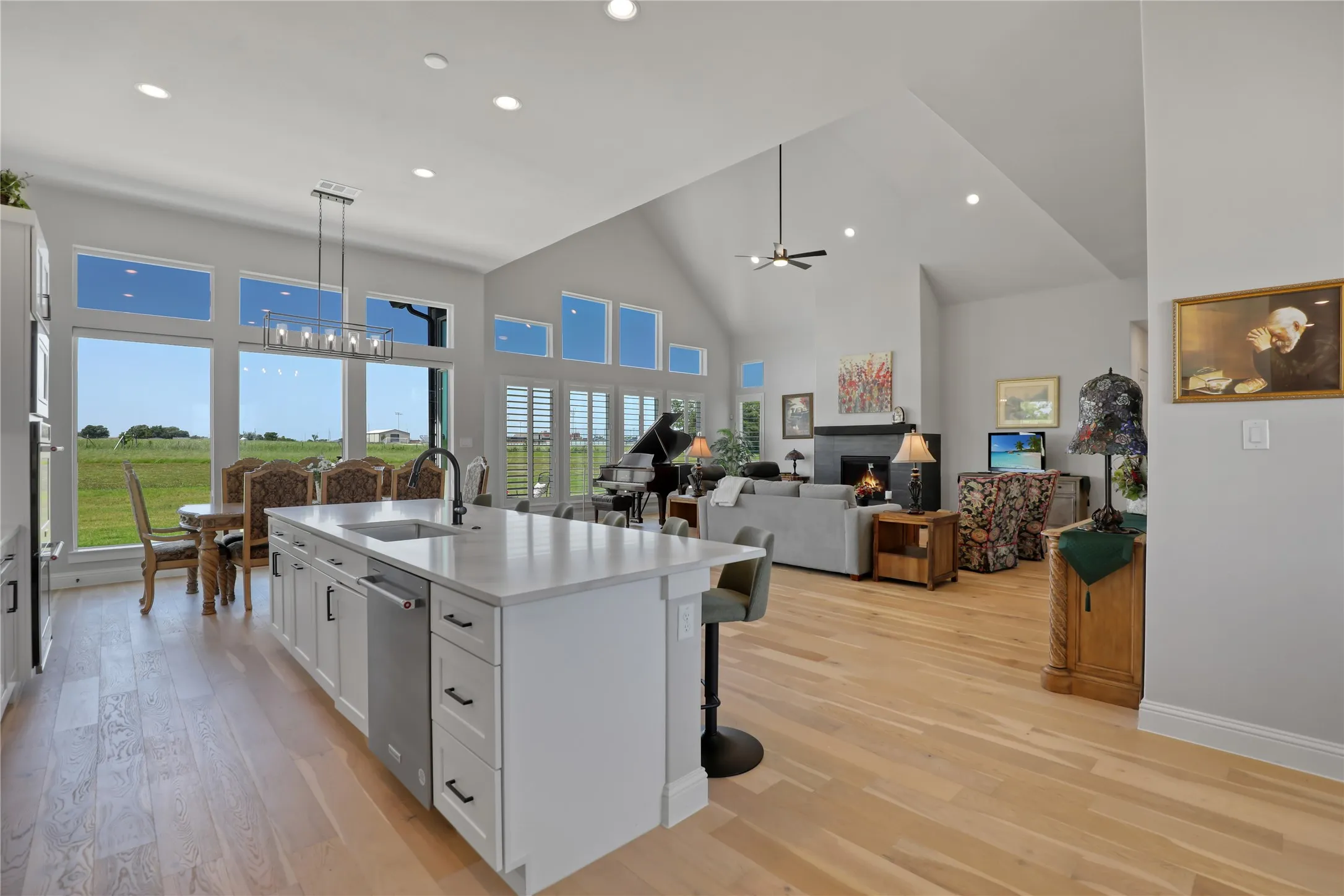 Kitchen with open floor plan, high vaulted ceiling, a kitchen island with sink, white cabinets, and a lit fireplace