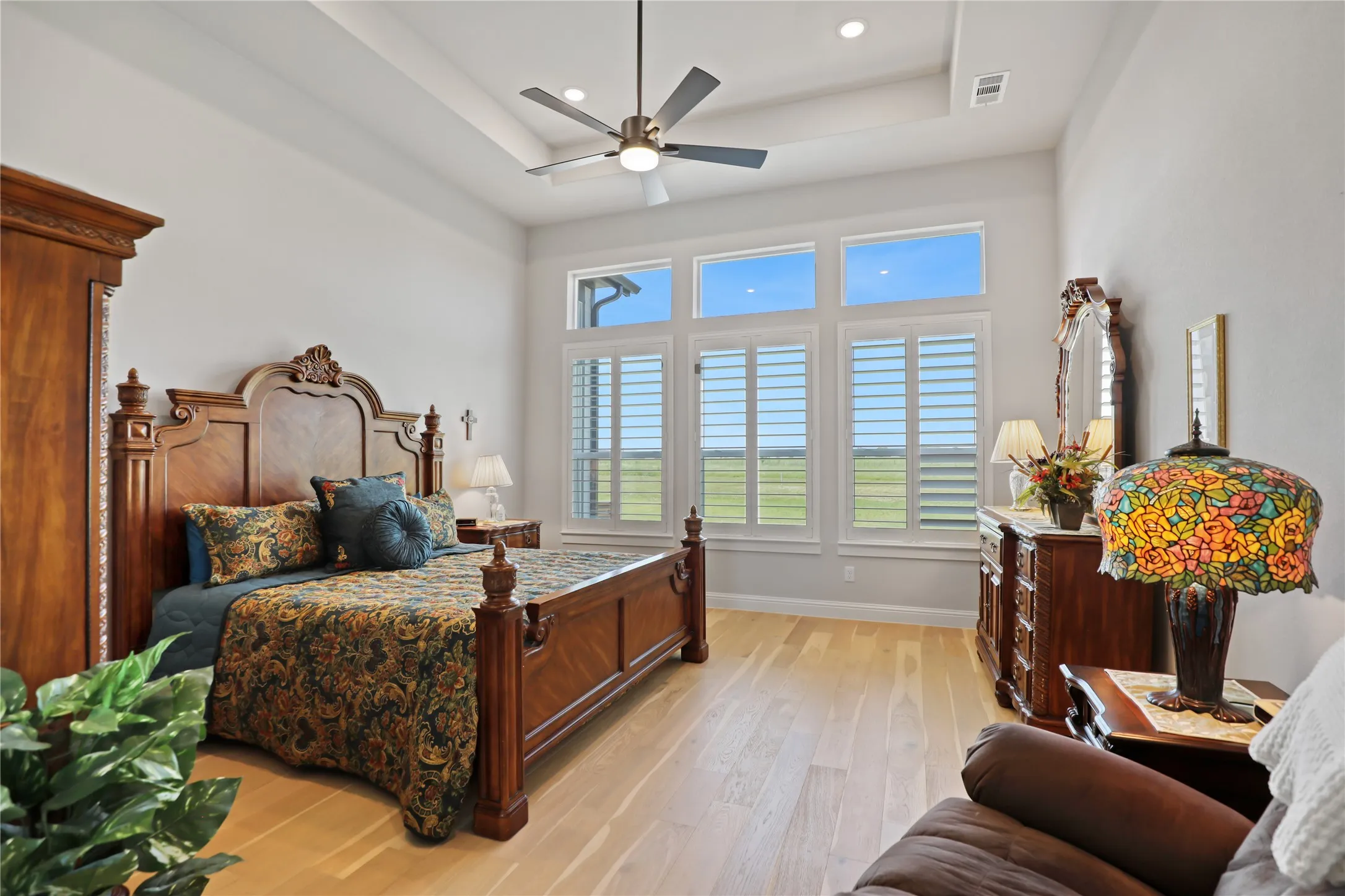 Bedroom with a tray ceiling, light wood finished floors, ceiling fan, and recessed lighting
