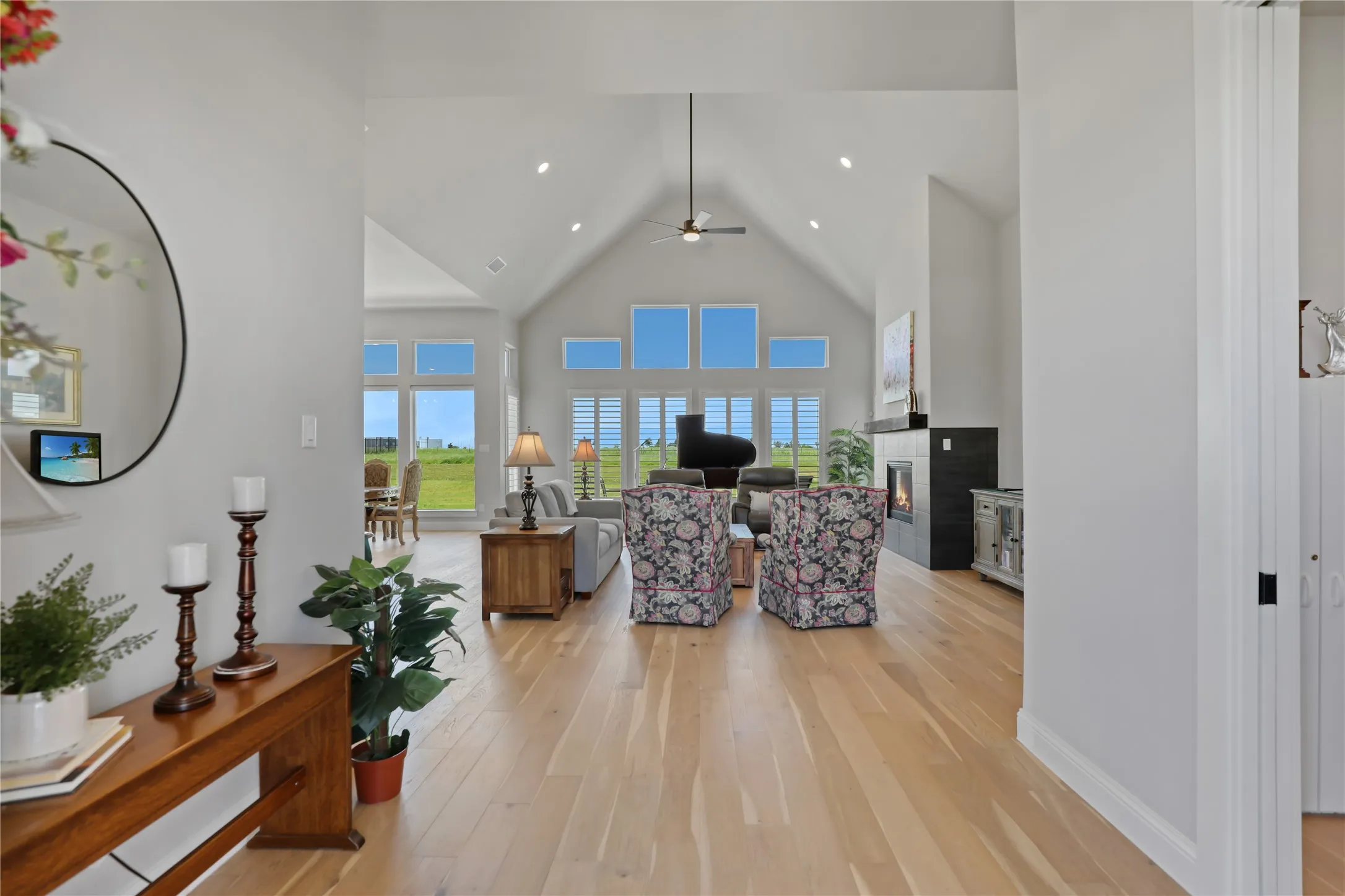 Living room with high vaulted ceiling, a glass covered fireplace, light wood-style flooring, a ceiling fan, and recessed lighting