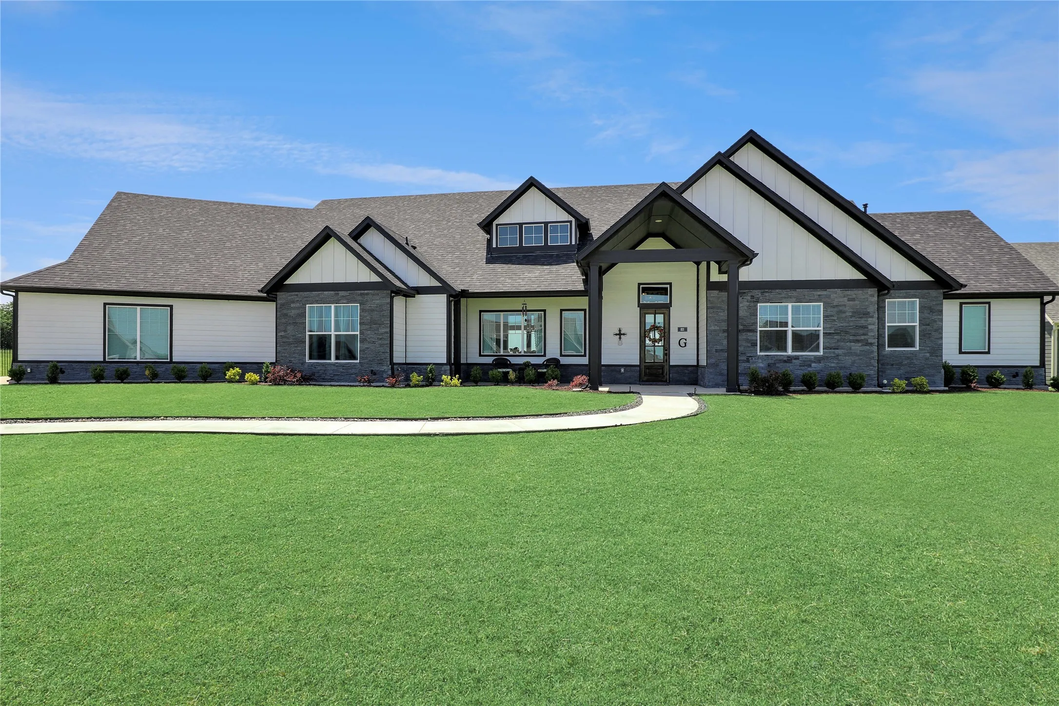 View of front of home with stone siding, roof with shingles, a front lawn, and board and batten siding