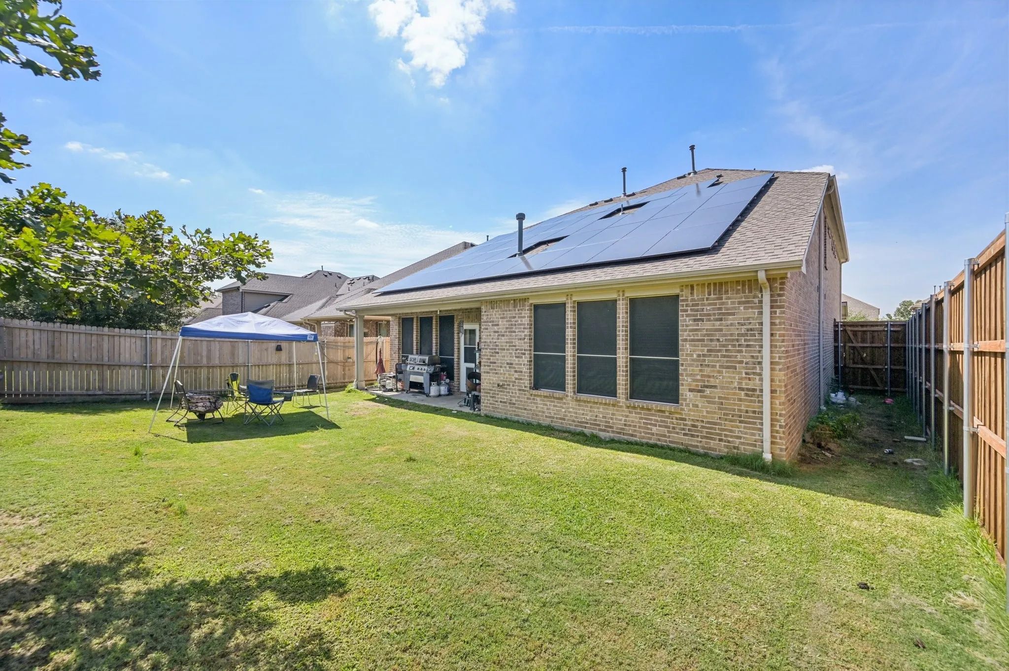 Rear view of property featuring a fenced backyard, brick siding, roof with shingles, and solar panels