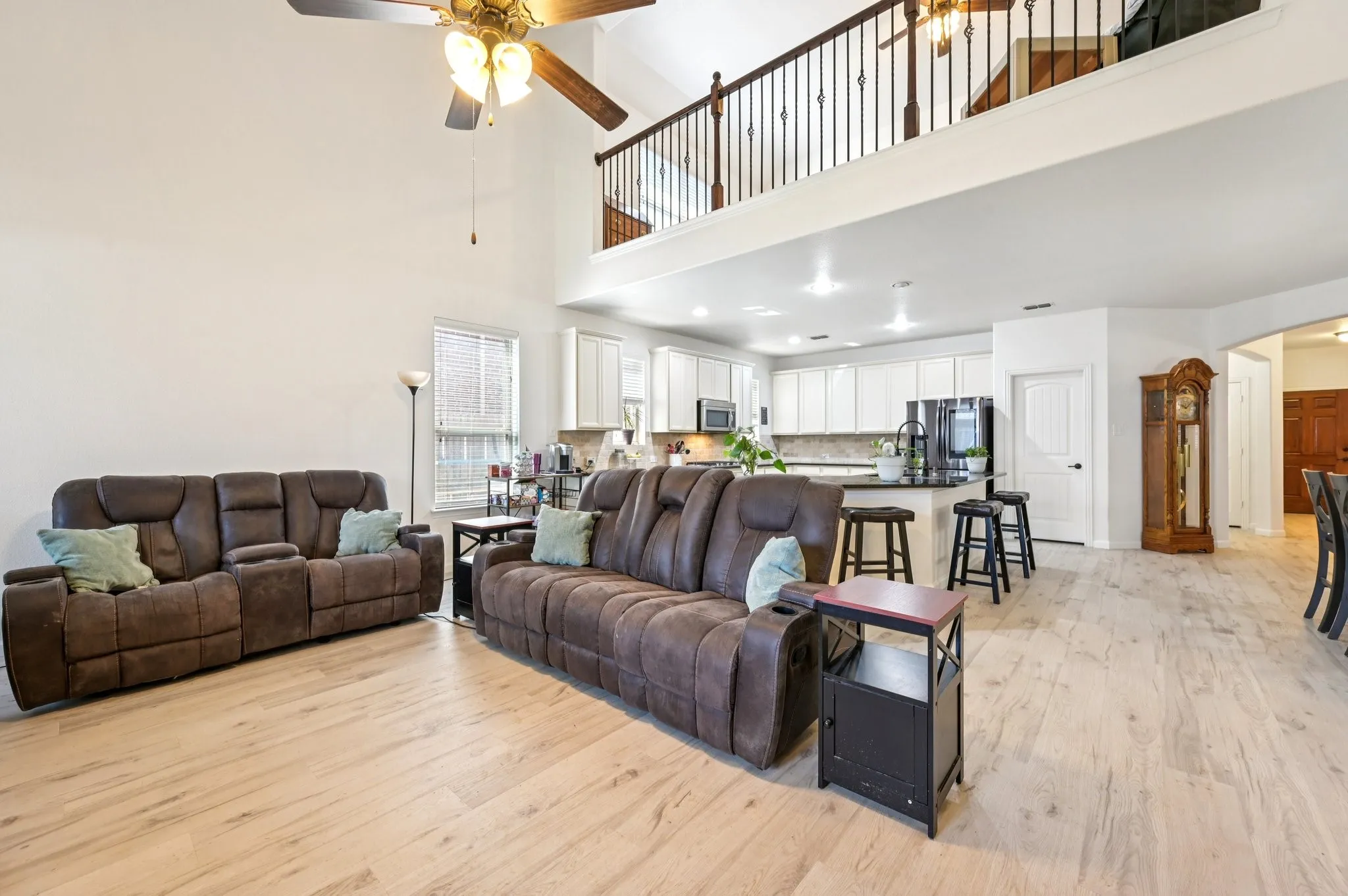 Living area with a ceiling fan, light wood-style flooring, and a towering ceiling
