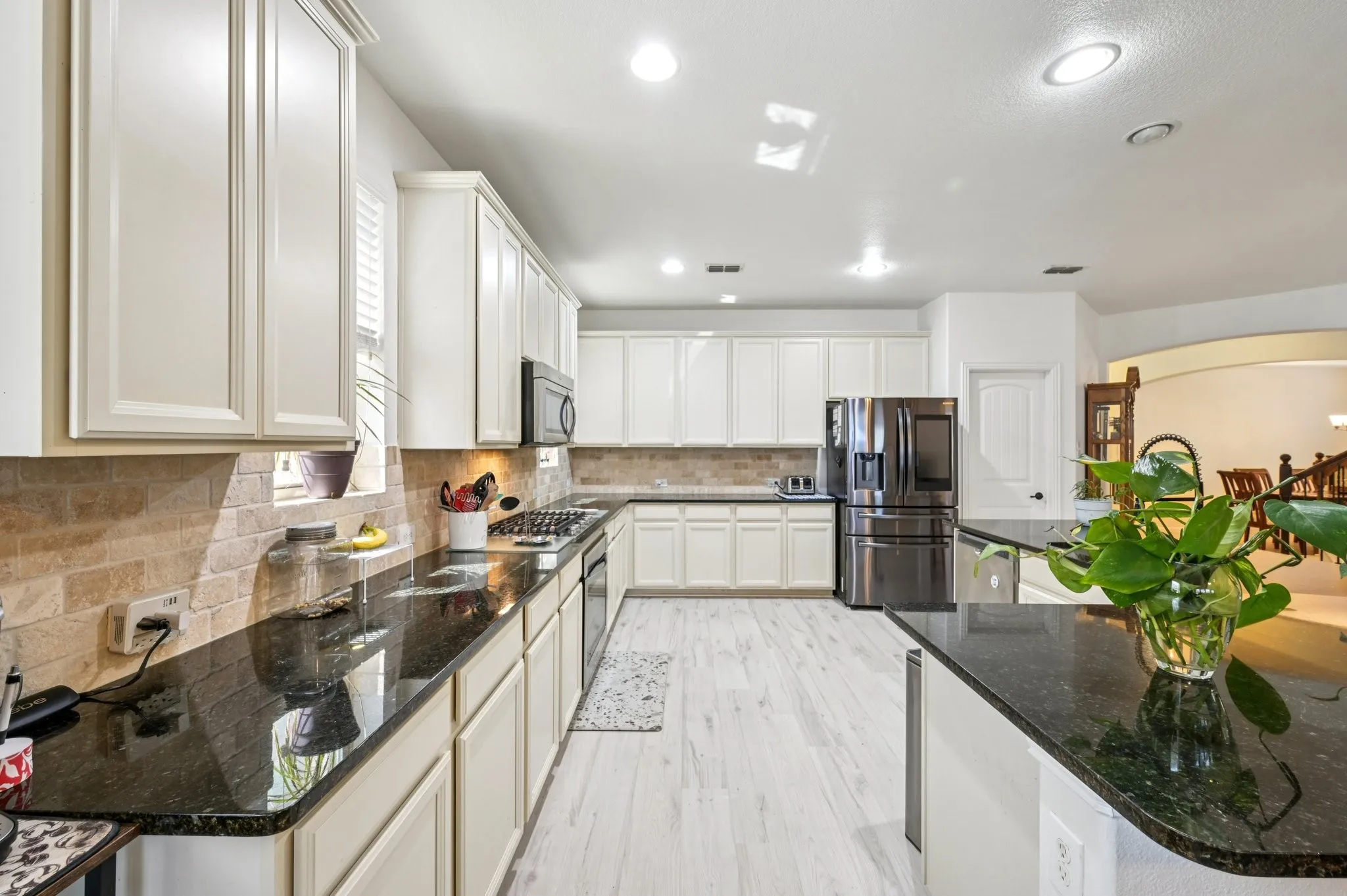 Kitchen with dark stone countertops, backsplash, stainless steel appliances, recessed lighting, and light wood-type flooring
