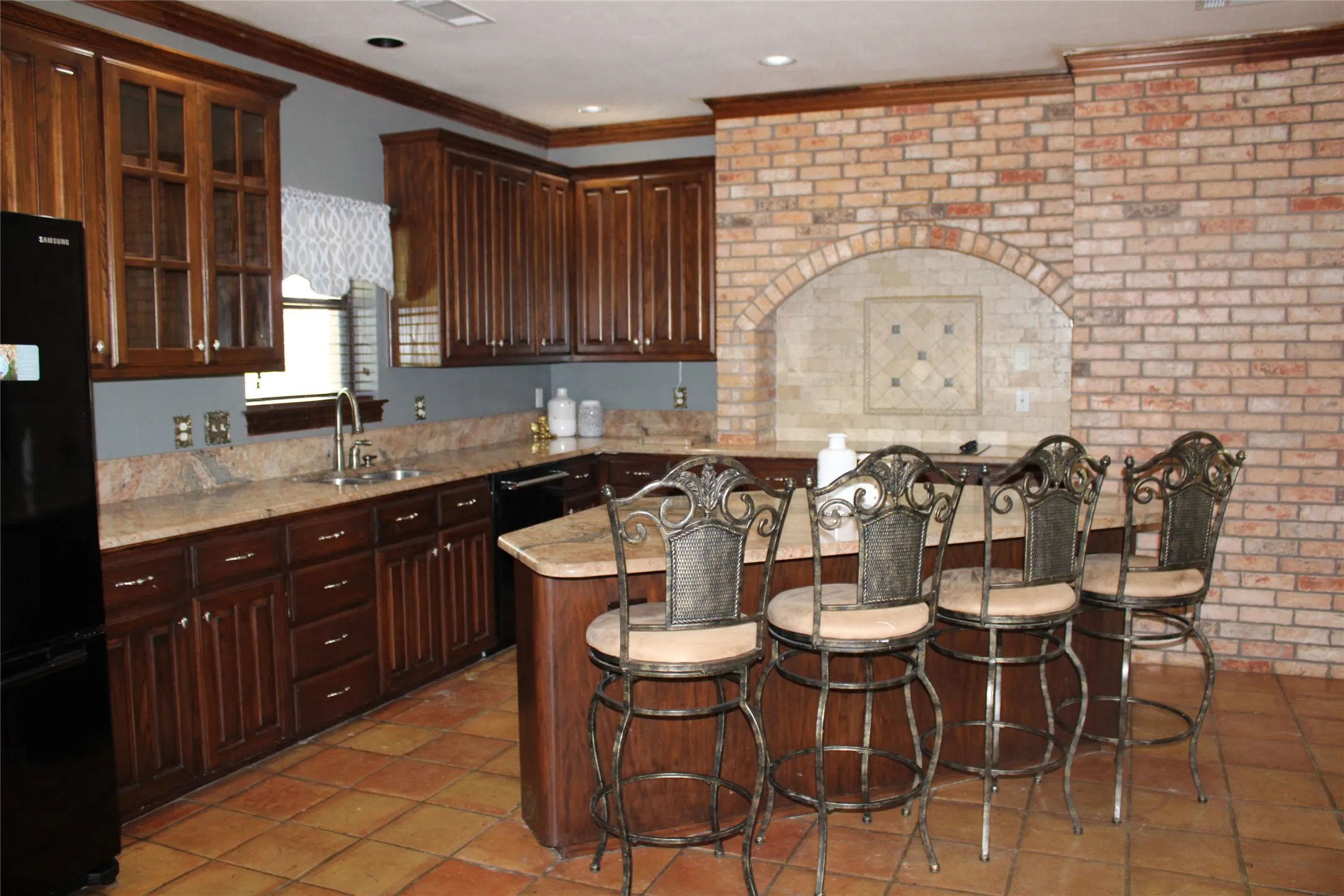 Kitchen featuring tile patterned flooring, brick wall, sink, and black fridge