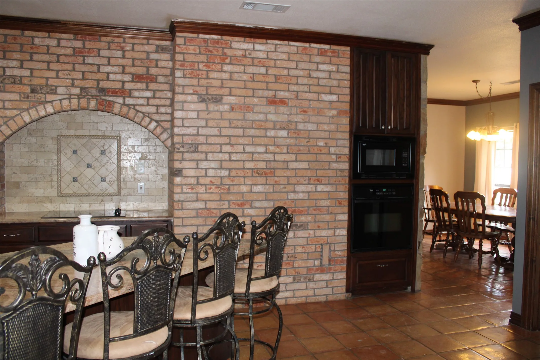 Tiled dining area with brick fireplace wall, a notable chandelier, and ornamental molding