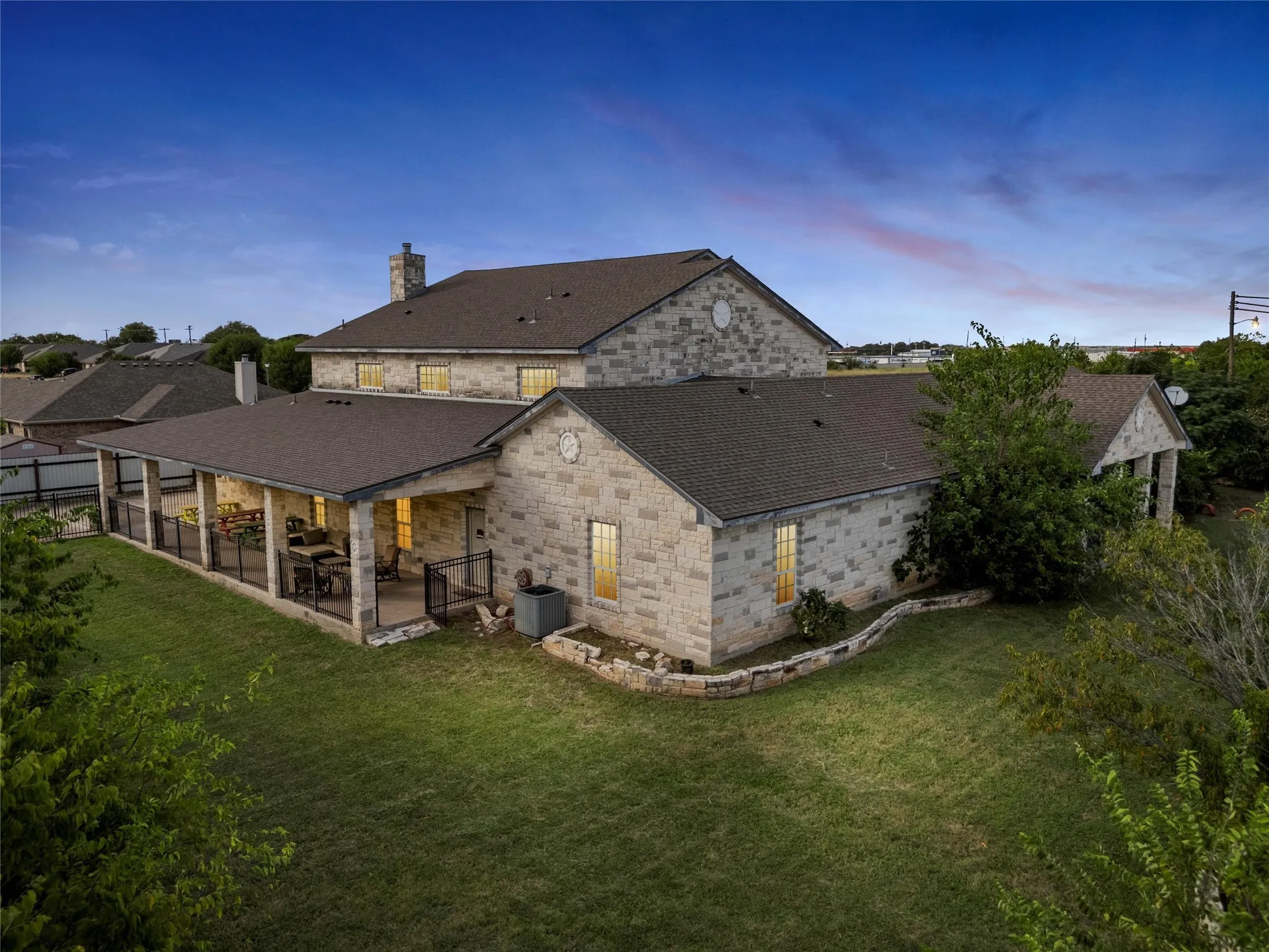 Back of property at dusk with a patio, a chimney, a yard, roof with shingles, and stone siding