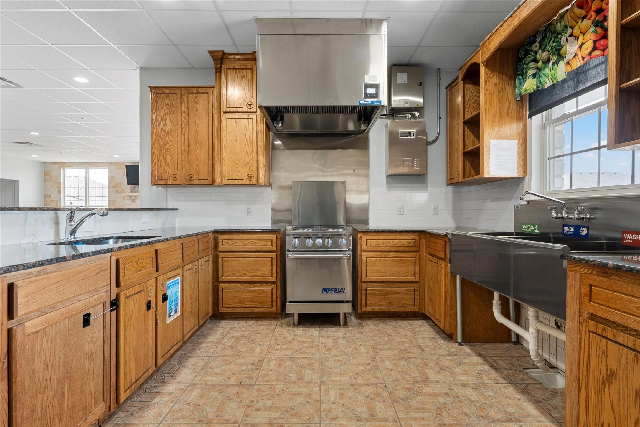 Kitchen featuring brown cabinets, dark stone countertops, open shelves, stainless steel range oven, and exhaust hood