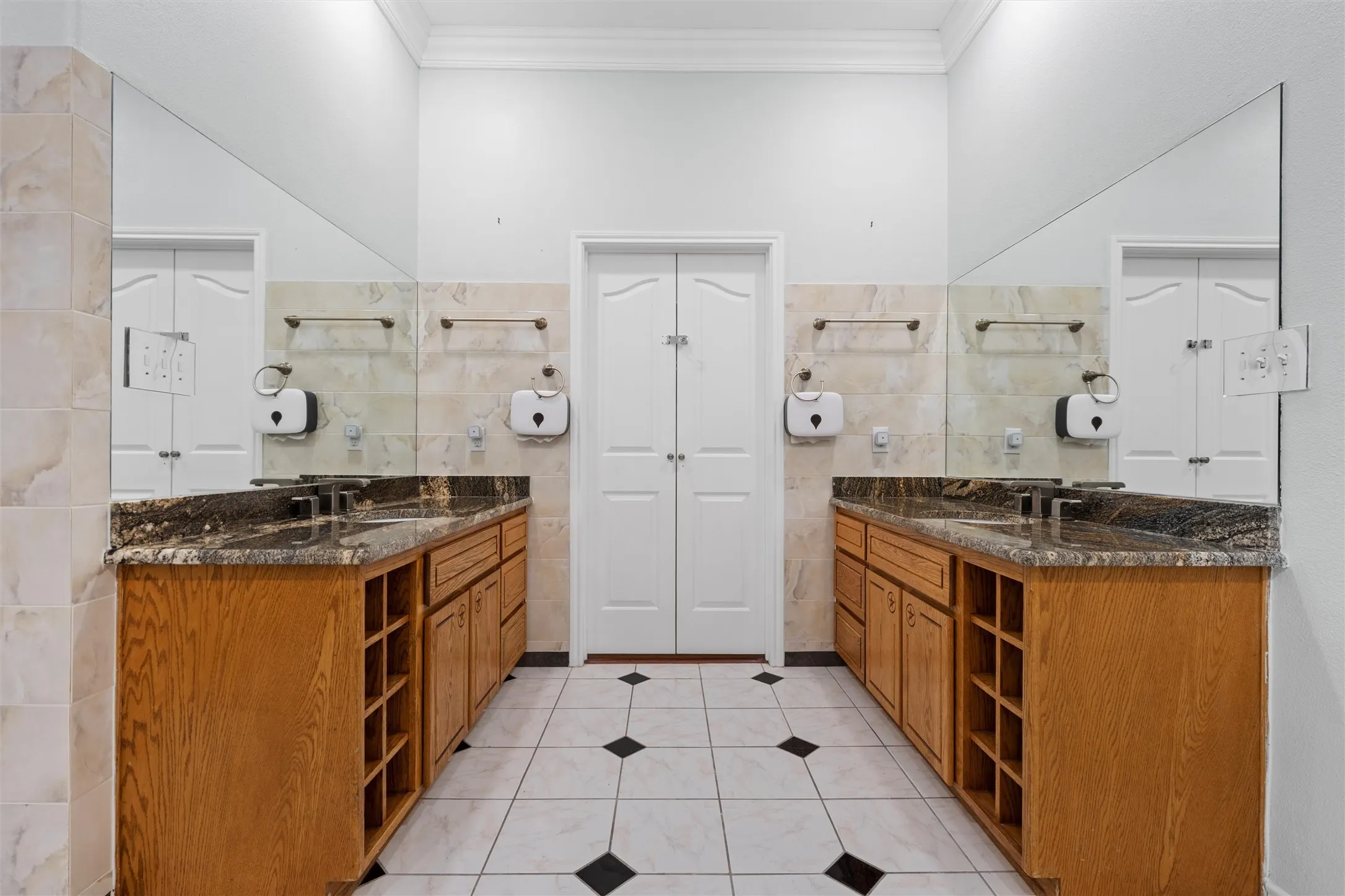 Bathroom with tile walls, two vanities, light tile patterned floors, crown molding, and a closet