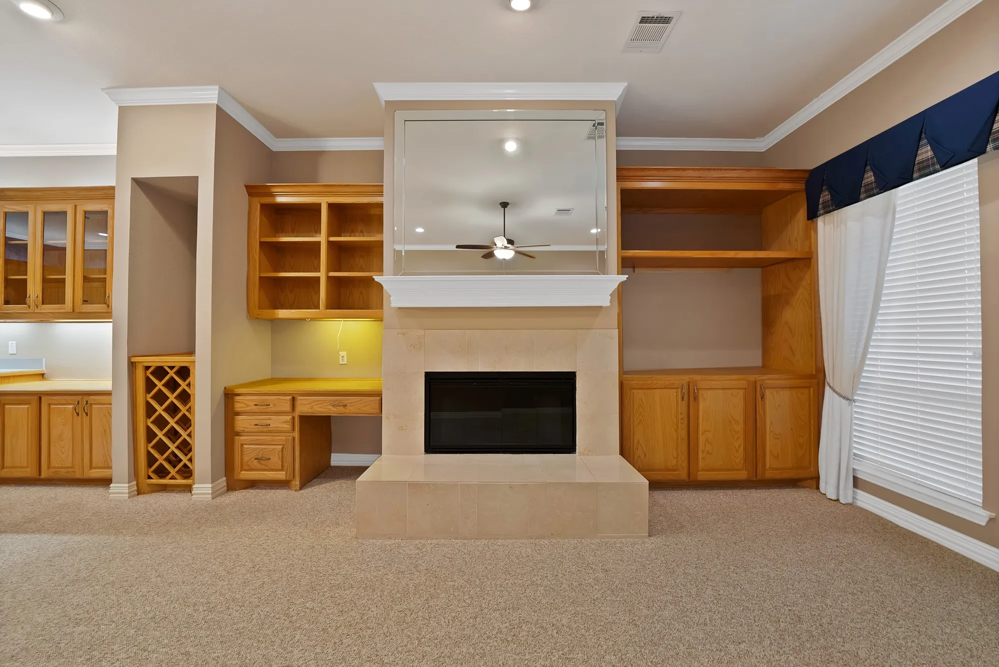 Unfurnished living room with built in desk, light carpet, ornamental molding, a tile fireplace, and a ceiling fan