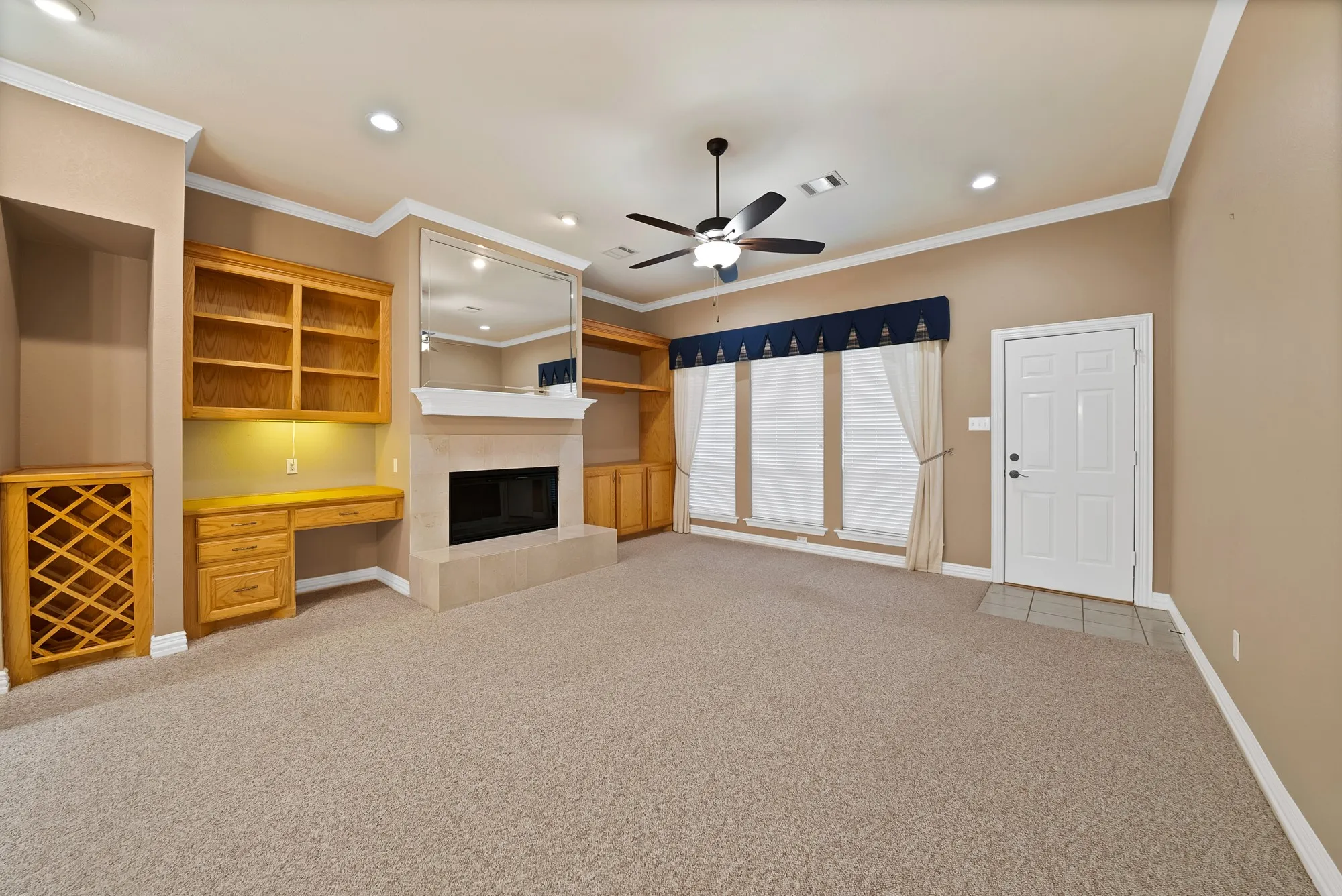 Unfurnished living room with built in study area, a fireplace, crown molding, light colored carpet, and recessed lighting