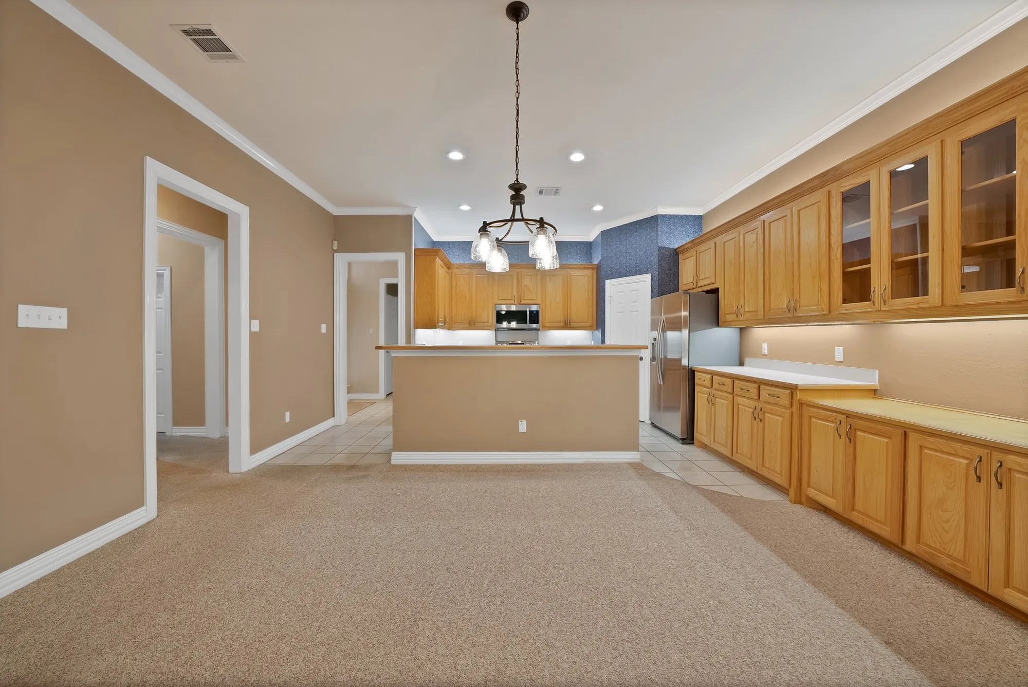 Kitchen featuring glass insert cabinets, hanging light fixtures, light carpet, stainless steel appliances, and crown molding