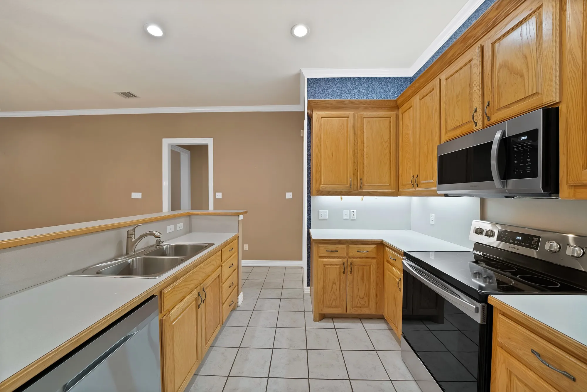 Kitchen with stainless steel appliances, crown molding, light tile patterned floors, light countertops, and recessed lighting