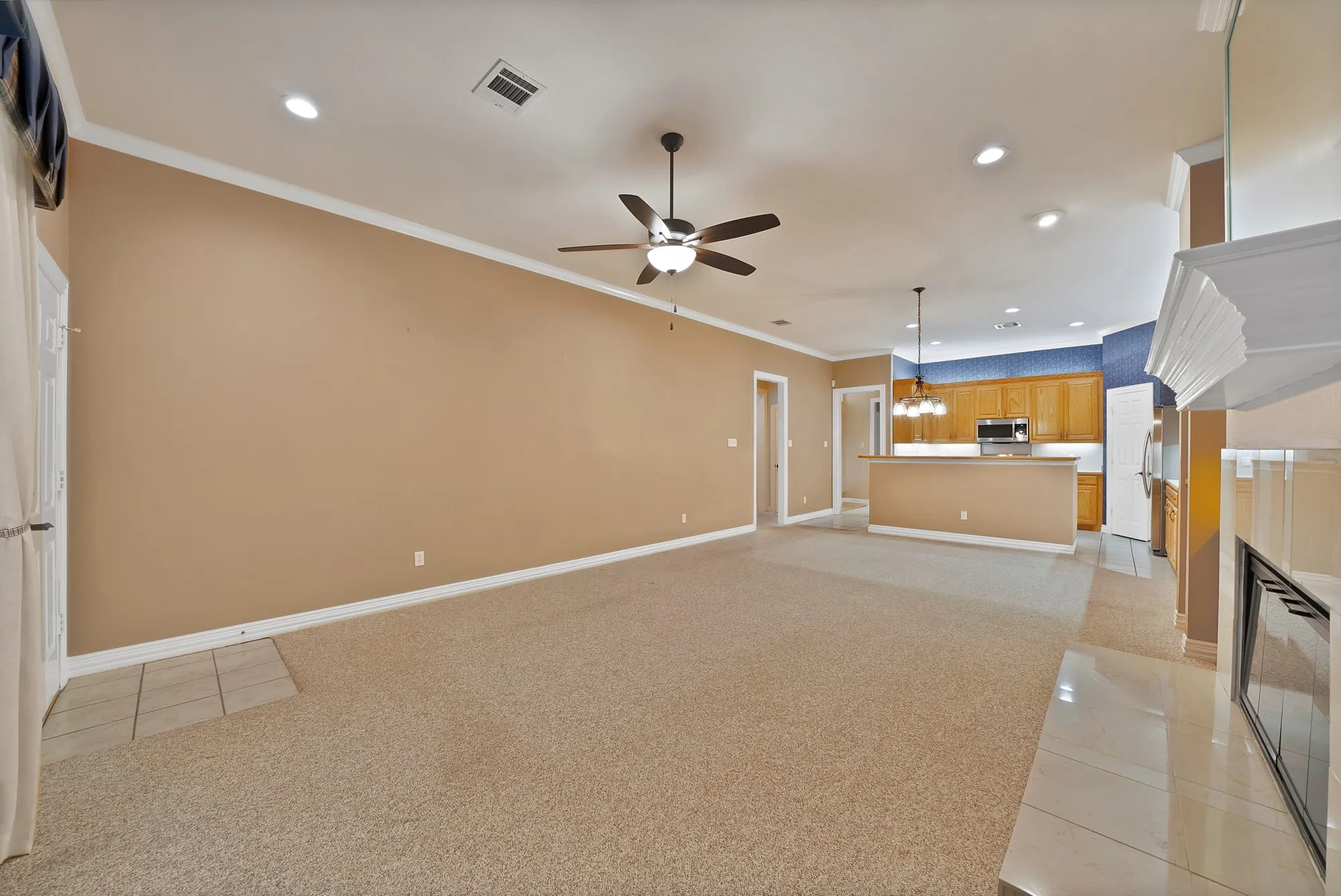 Unfurnished living room featuring crown molding, light tile patterned floors, light colored carpet, a glass covered fireplace, and recessed lighting