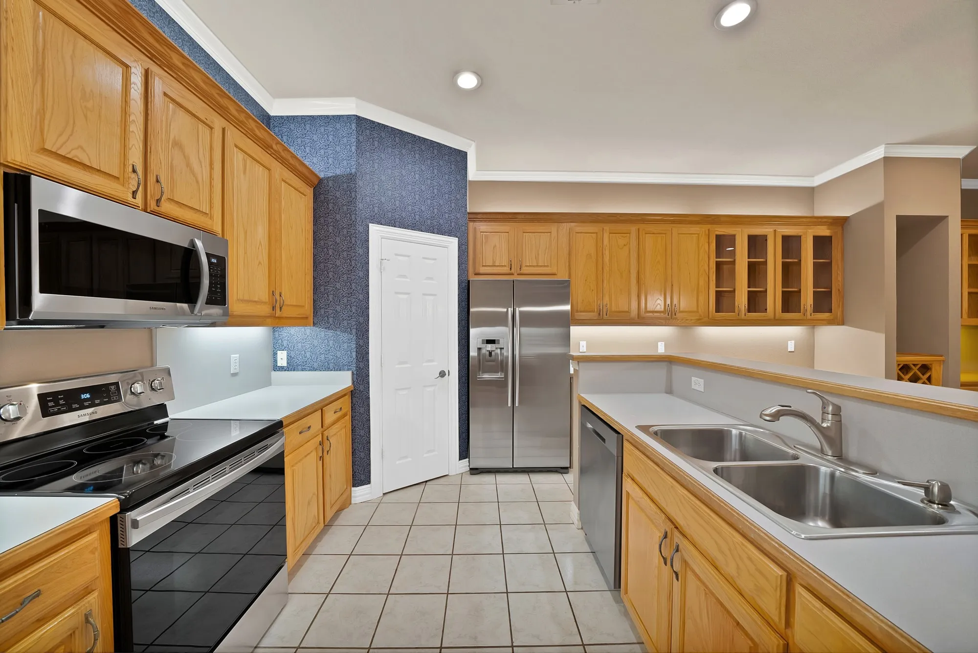 Kitchen with appliances with stainless steel finishes, ornamental molding, glass insert cabinets, light tile patterned floors, and light countertops