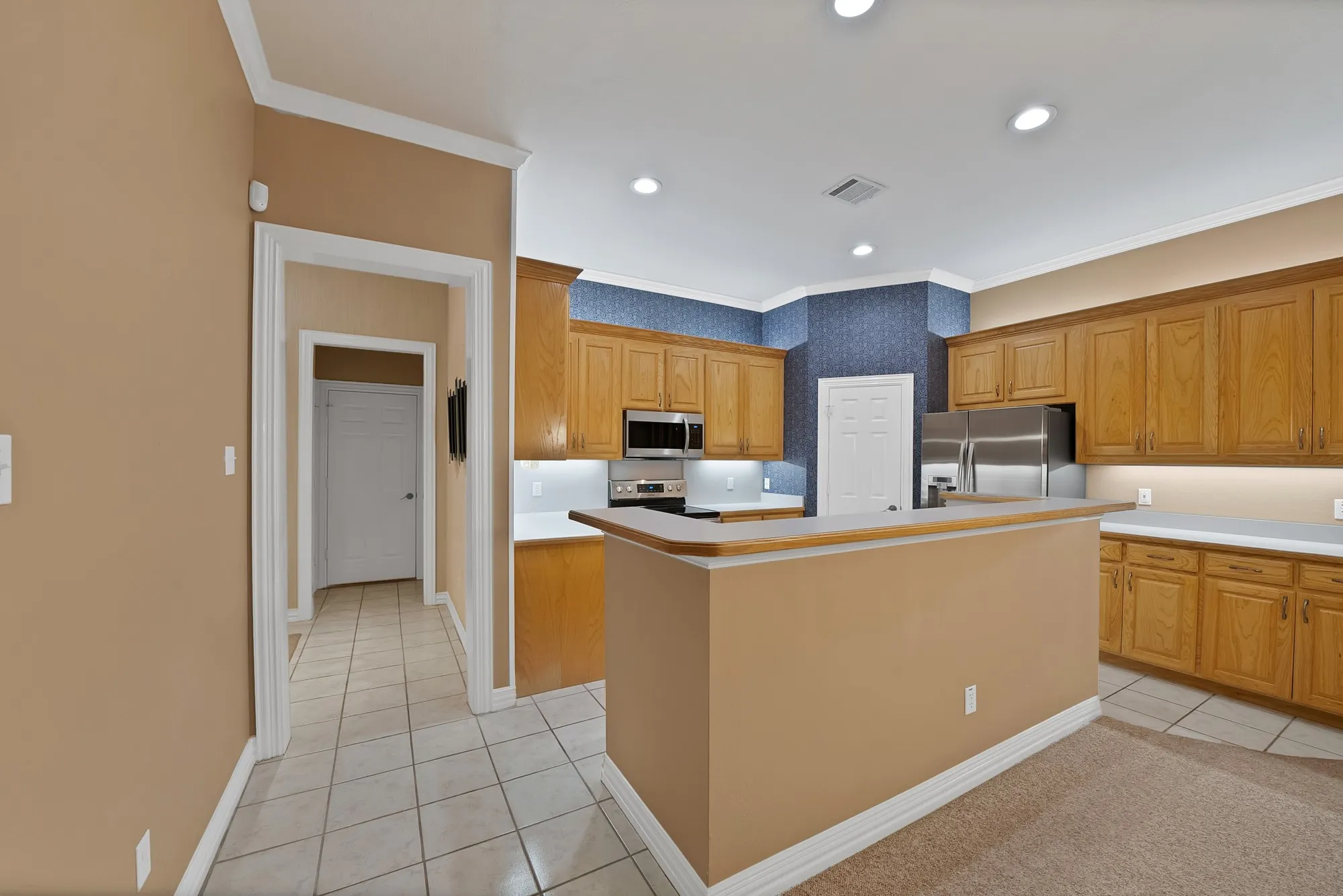 Kitchen featuring light tile patterned flooring, crown molding, light countertops, appliances with stainless steel finishes, and a kitchen island