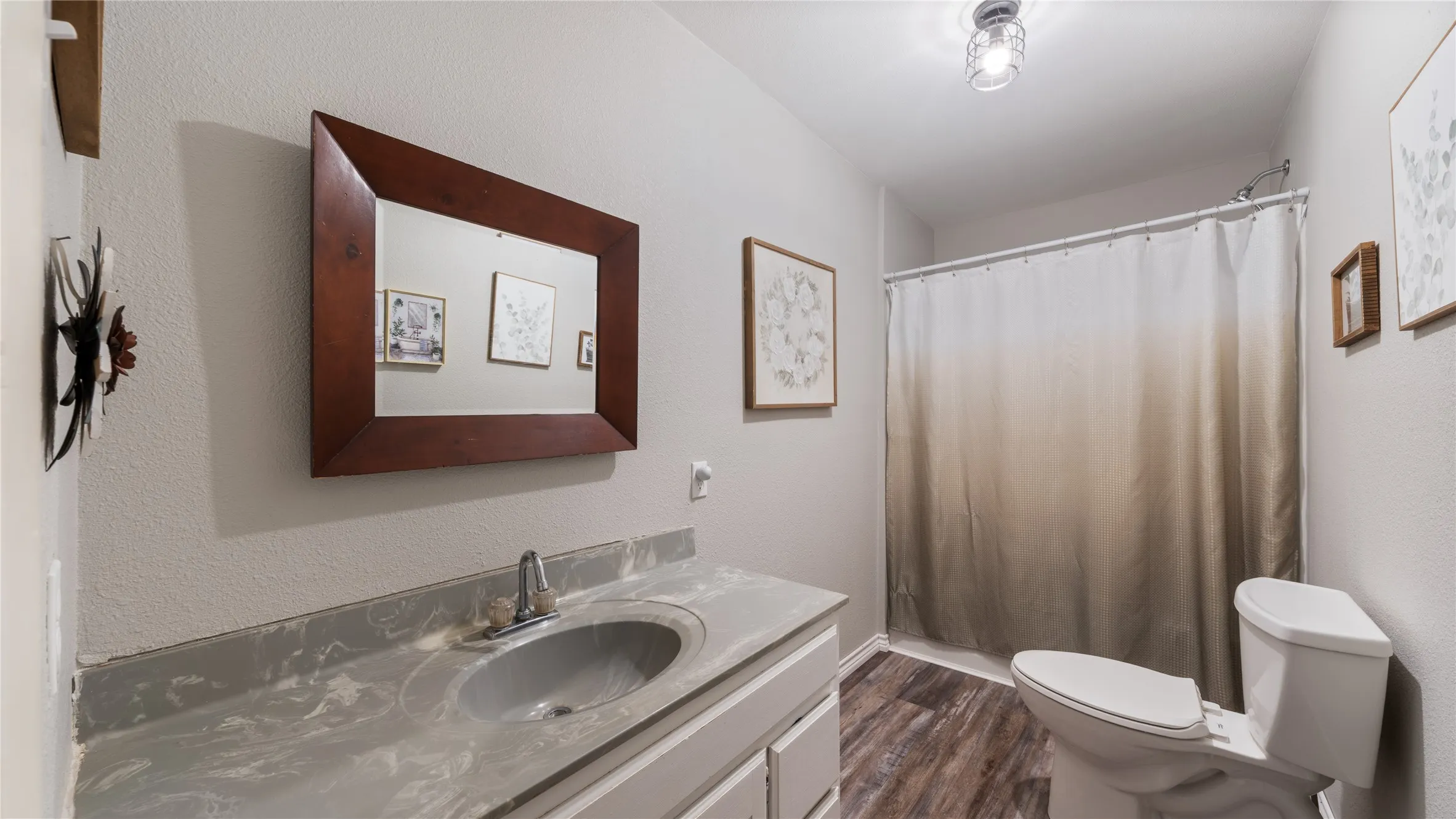Full bathroom featuring vanity, dark wood finished floors, a textured wall, and a shower with curtain