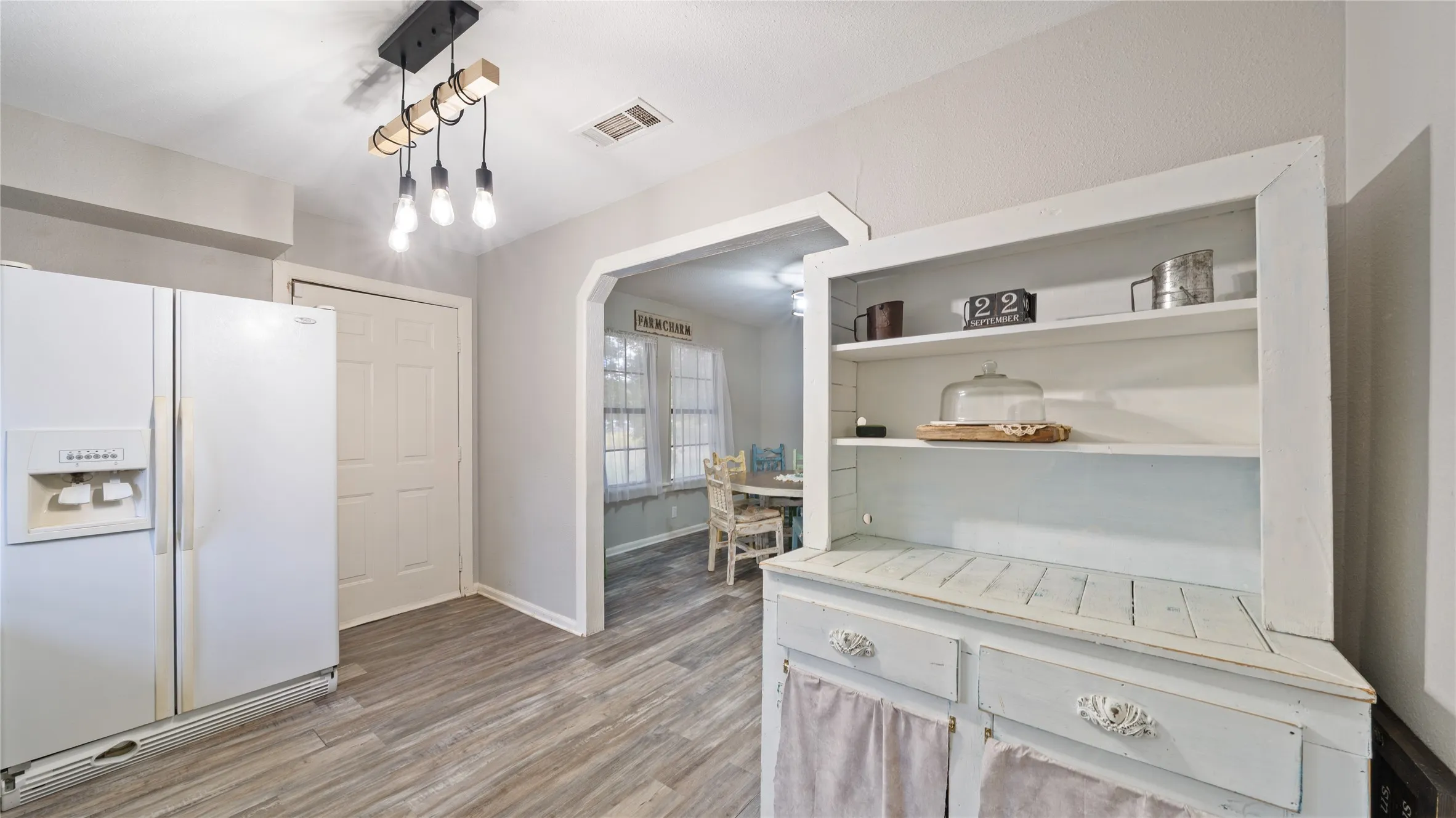 Kitchen with white refrigerator with ice dispenser, light wood finished floors, open shelves, pendant lighting, and light countertops