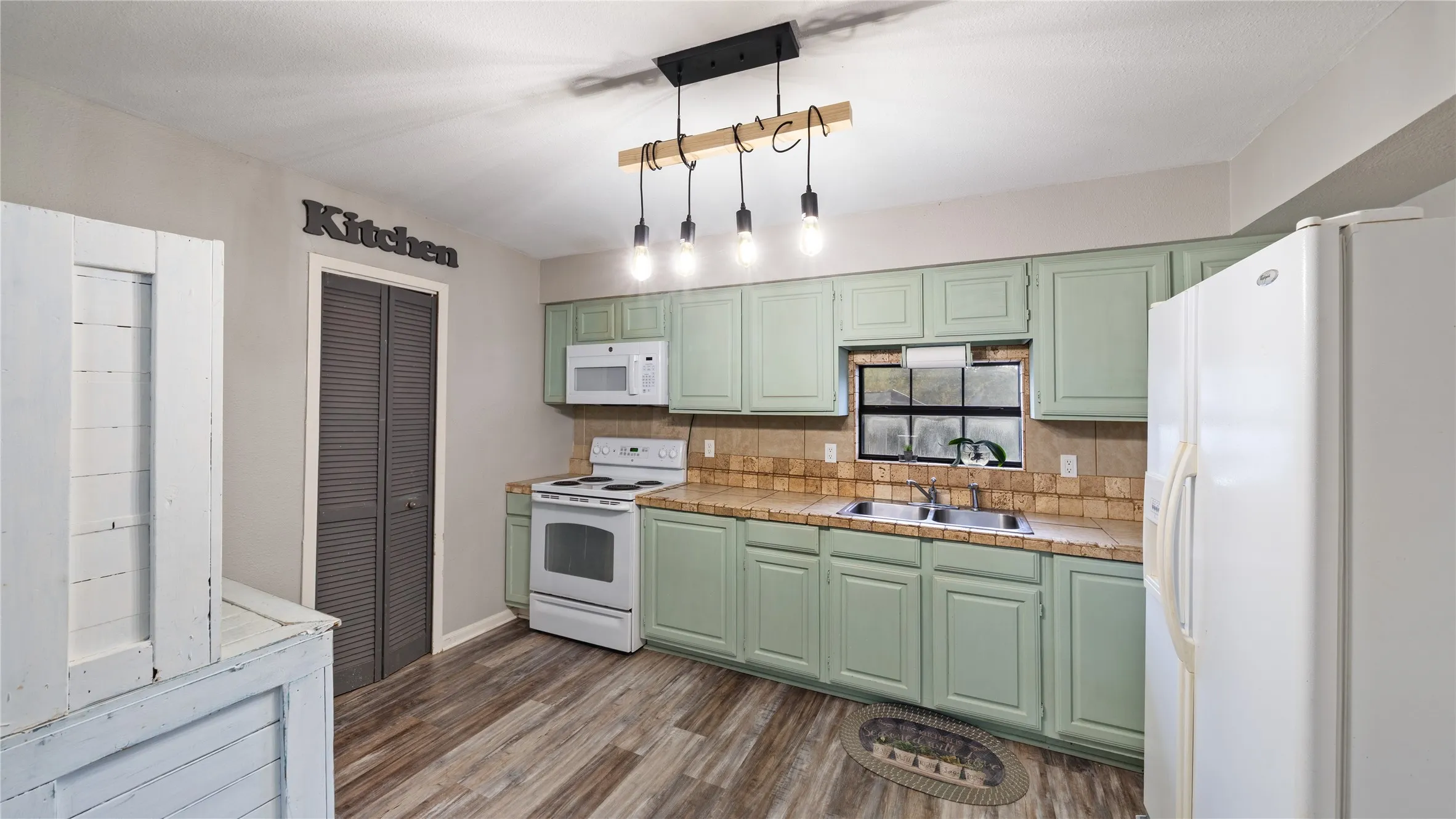Kitchen featuring green cabinetry, white appliances, dark wood finished floors, backsplash, and hanging light fixtures