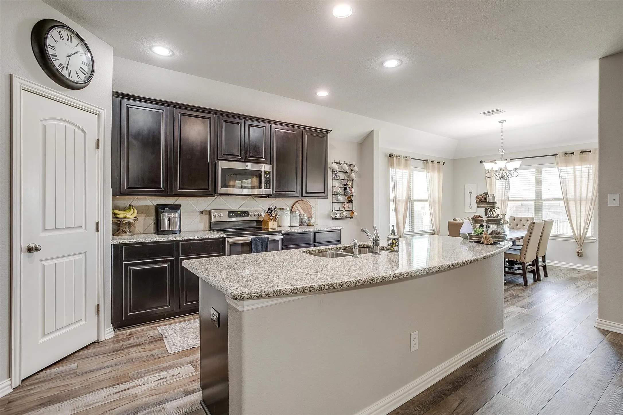 Kitchen featuring decorative backsplash, appliances with stainless steel finishes, light stone counters, light wood-style flooring, and recessed lighting