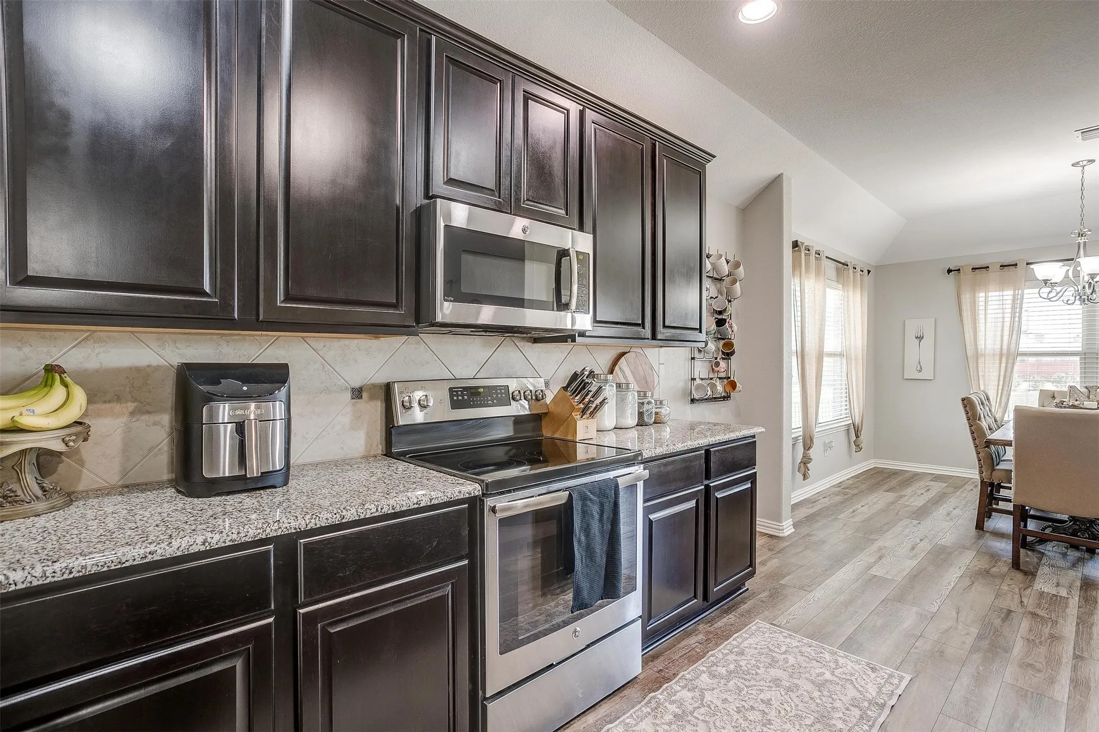 Kitchen with appliances with stainless steel finishes, light stone counters, light wood finished floors, tasteful backsplash, and decorative light fixtures