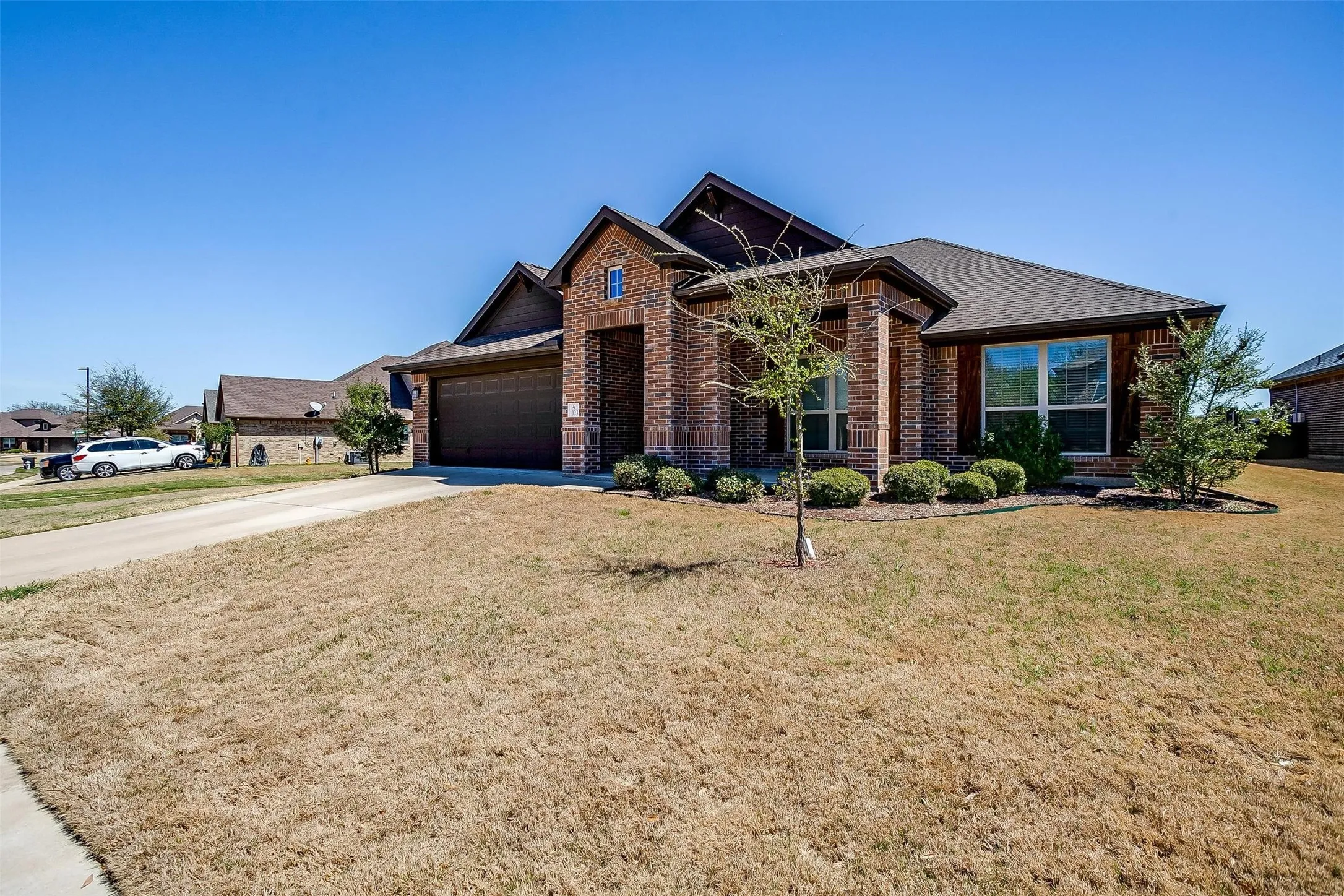View of front facade with brick siding, a front lawn, concrete driveway, a garage, and roof with shingles
