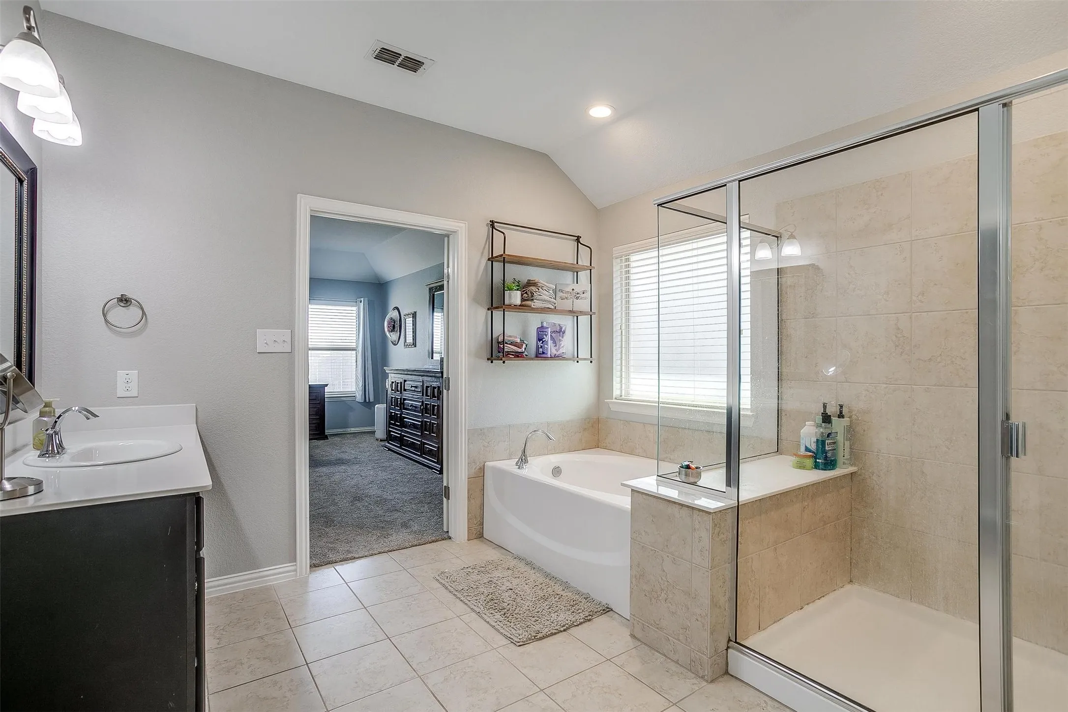 Ensuite bathroom with a garden tub, double vanity, light tile patterned flooring, vaulted ceiling, and a shower stall