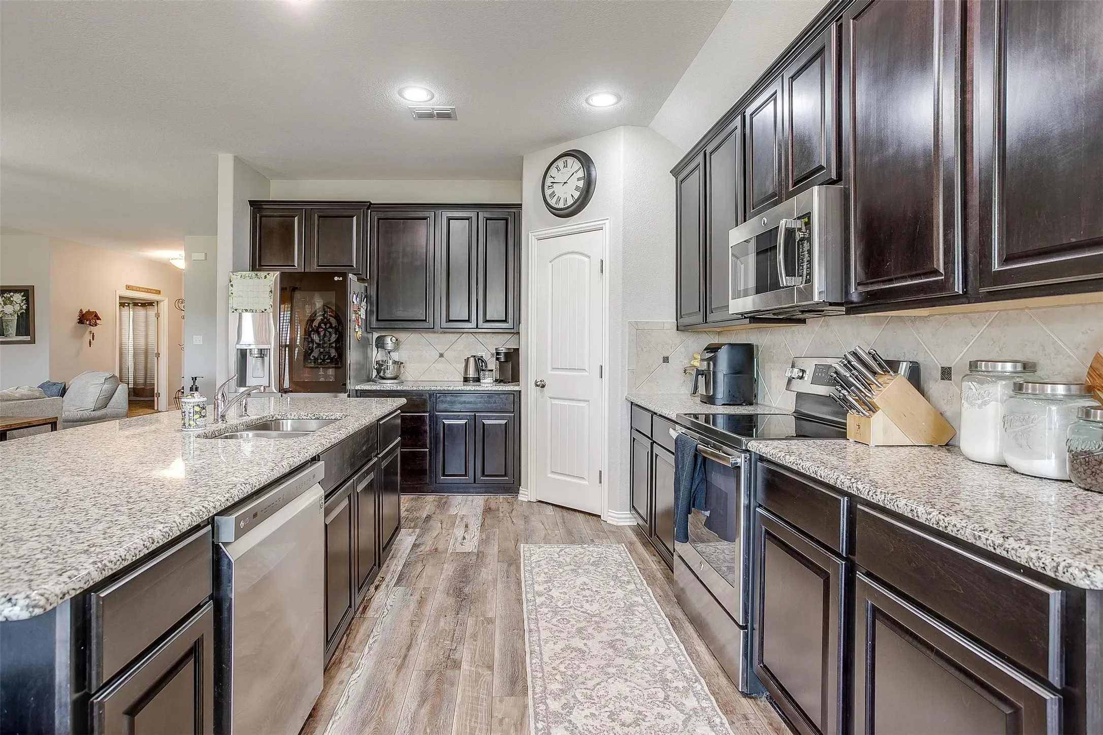 Kitchen featuring appliances with stainless steel finishes, light wood-style floors, decorative backsplash, light stone counters, and recessed lighting