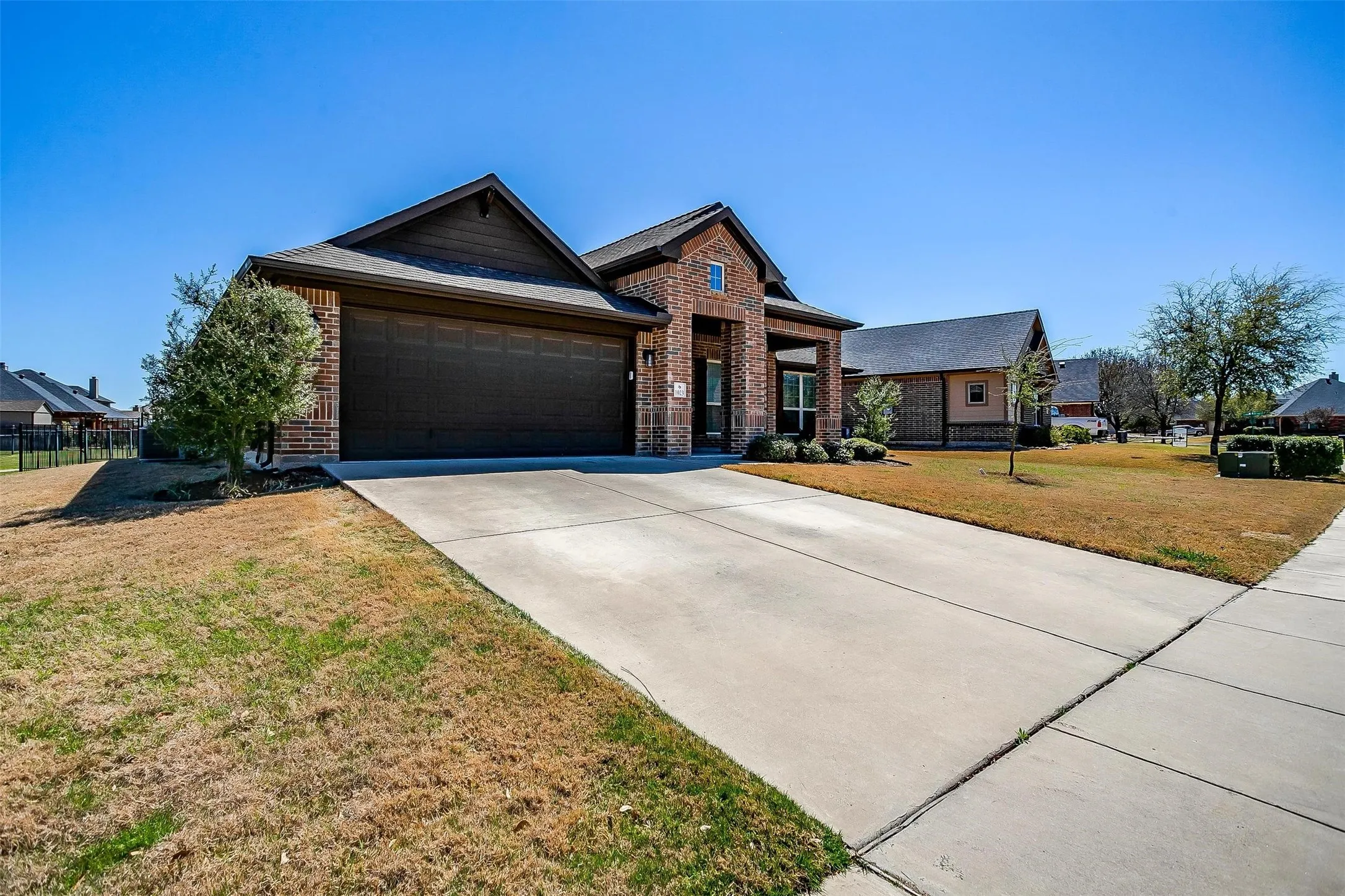 View of front facade with brick siding, driveway, a front lawn, an attached garage, and covered porch