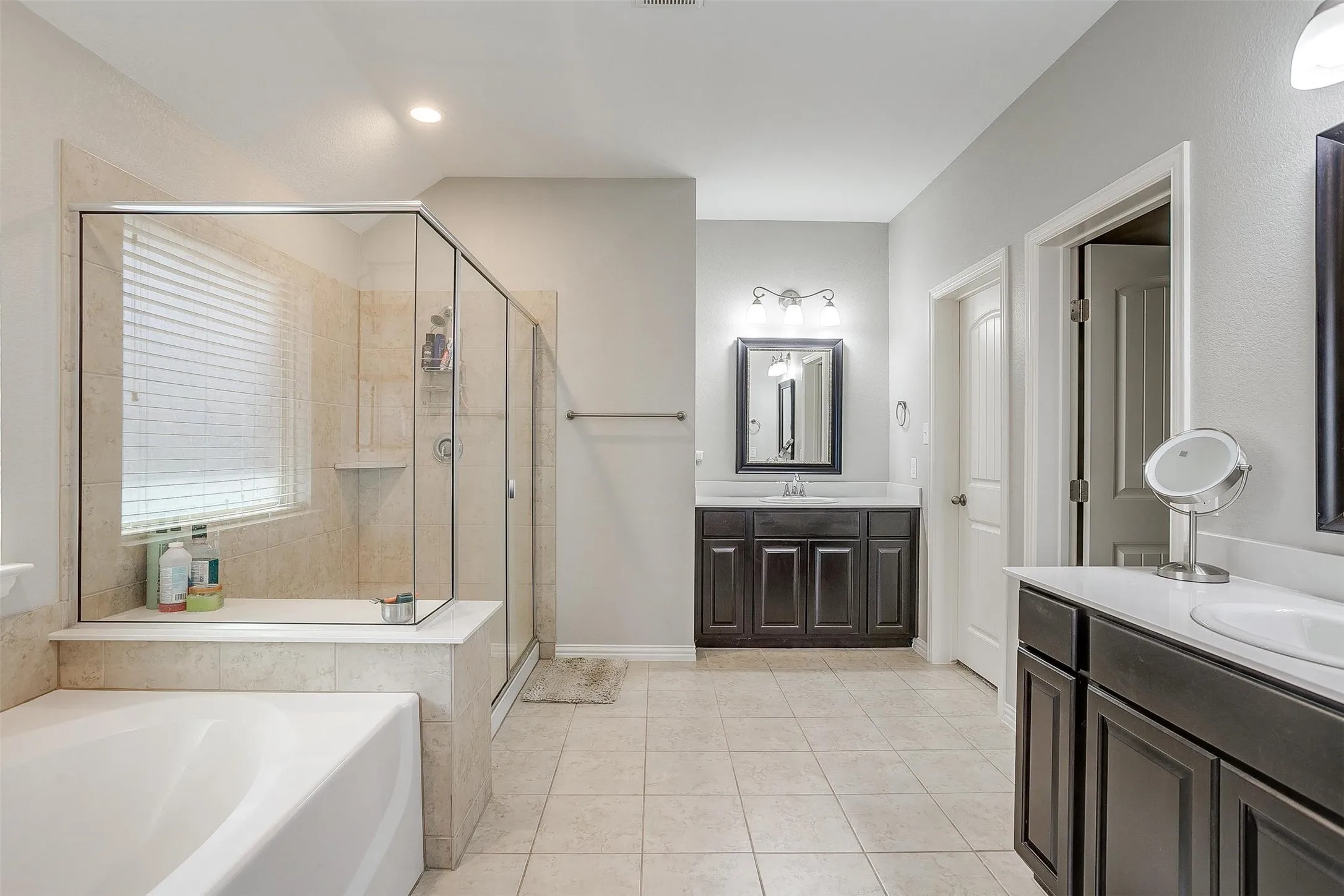 Full bathroom with light tile patterned flooring, two vanities, a garden tub, a shower stall, and recessed lighting
