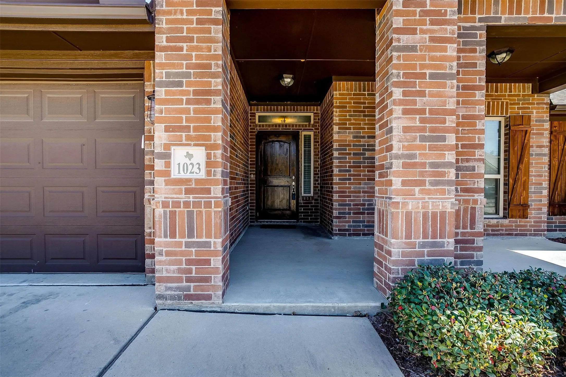 View of exterior entry with brick siding, a garage, and a porch