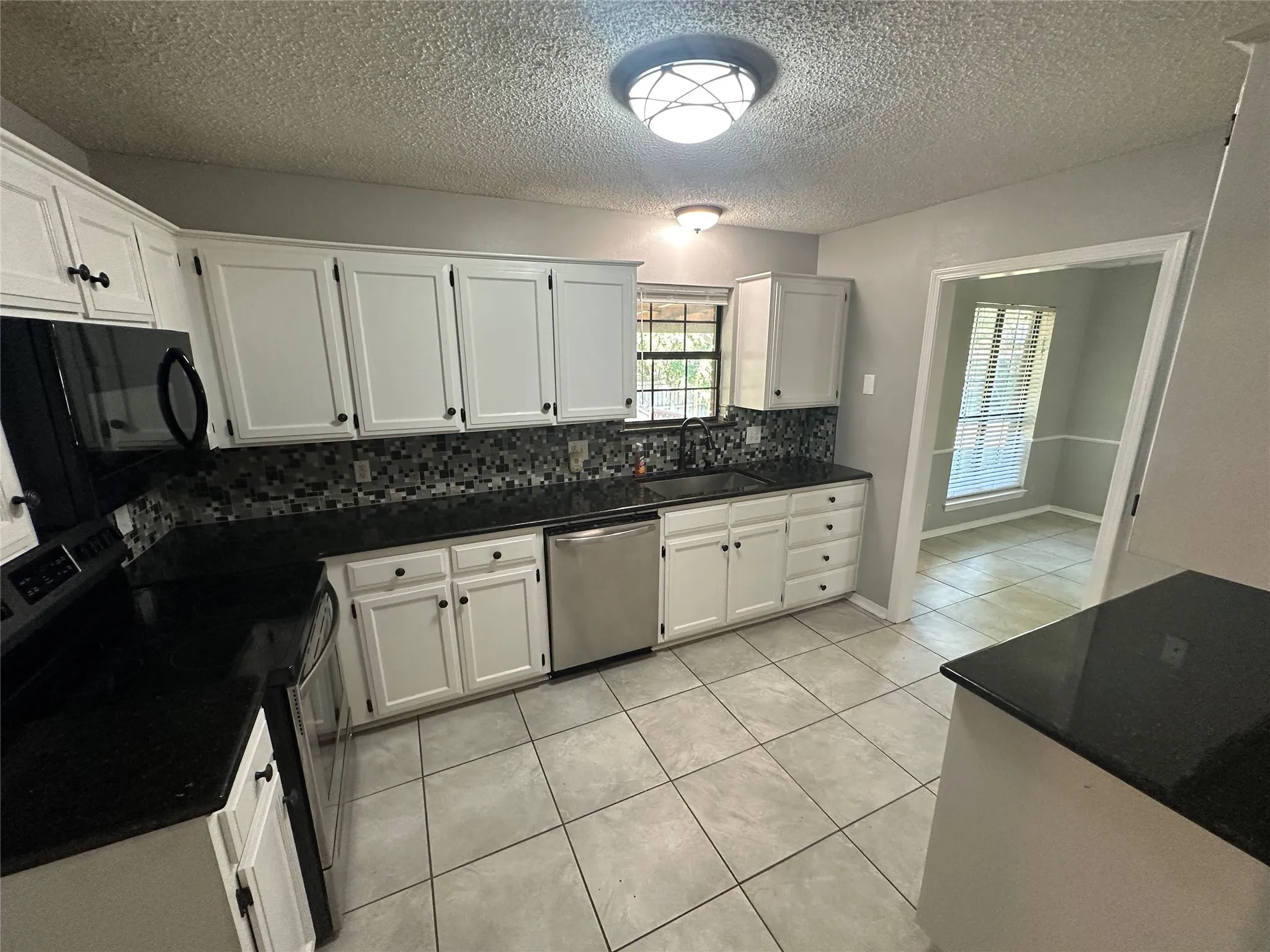 Kitchen with white cabinets, stainless steel appliances, decorative backsplash, light tile patterned floors, and a textured ceiling