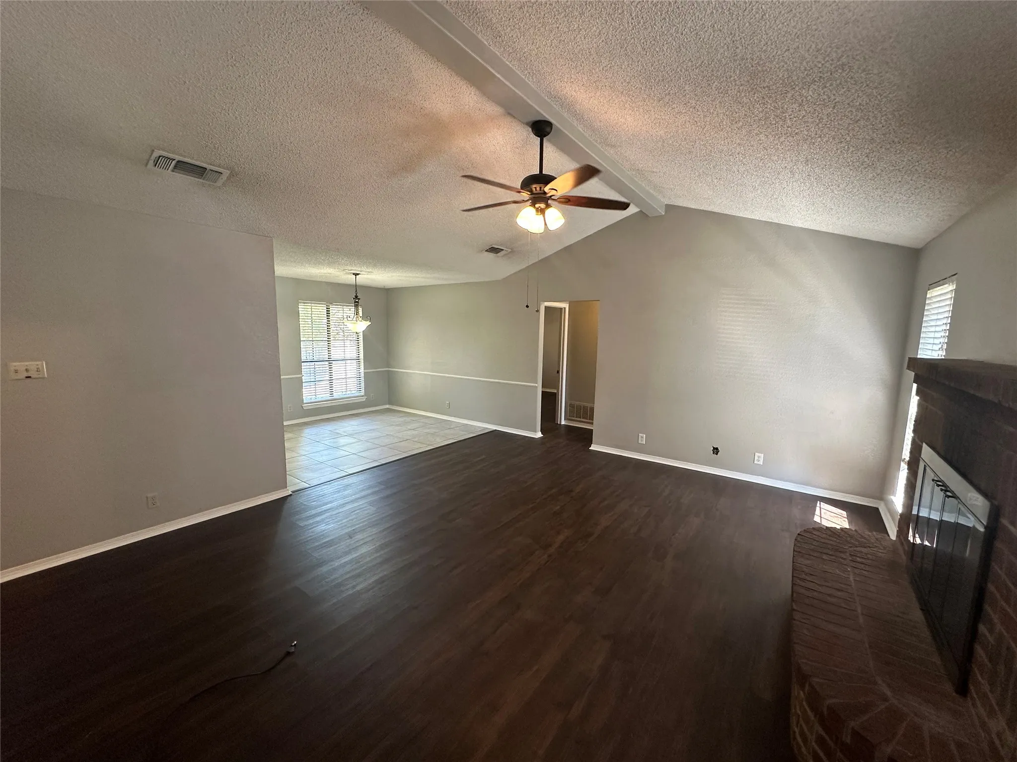 Unfurnished living room featuring dark wood finished floors, a chandelier, a fireplace, a textured ceiling, and a ceiling fan
