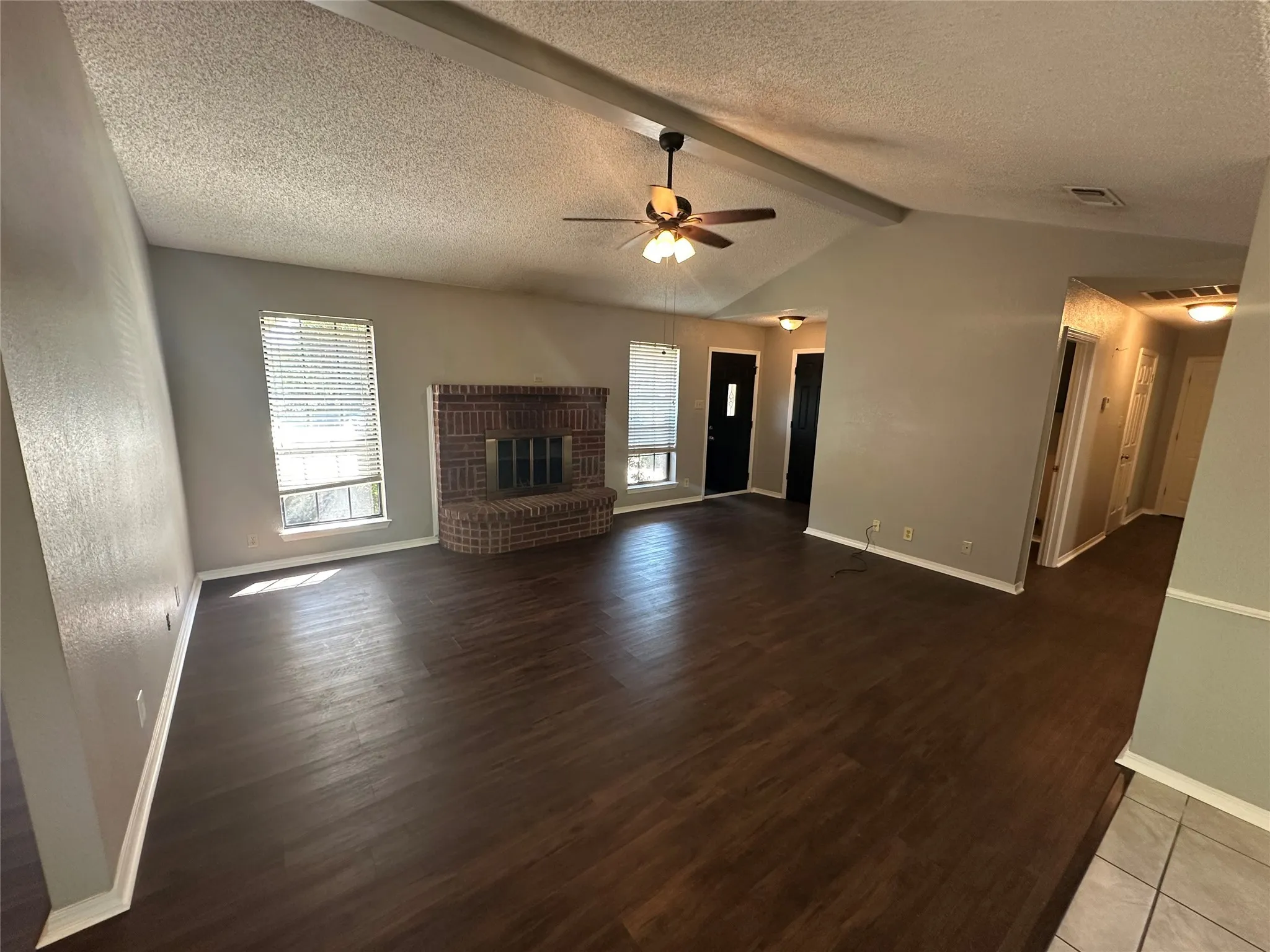 Unfurnished living room with a brick fireplace, dark wood-type flooring, a textured ceiling, and a ceiling fan