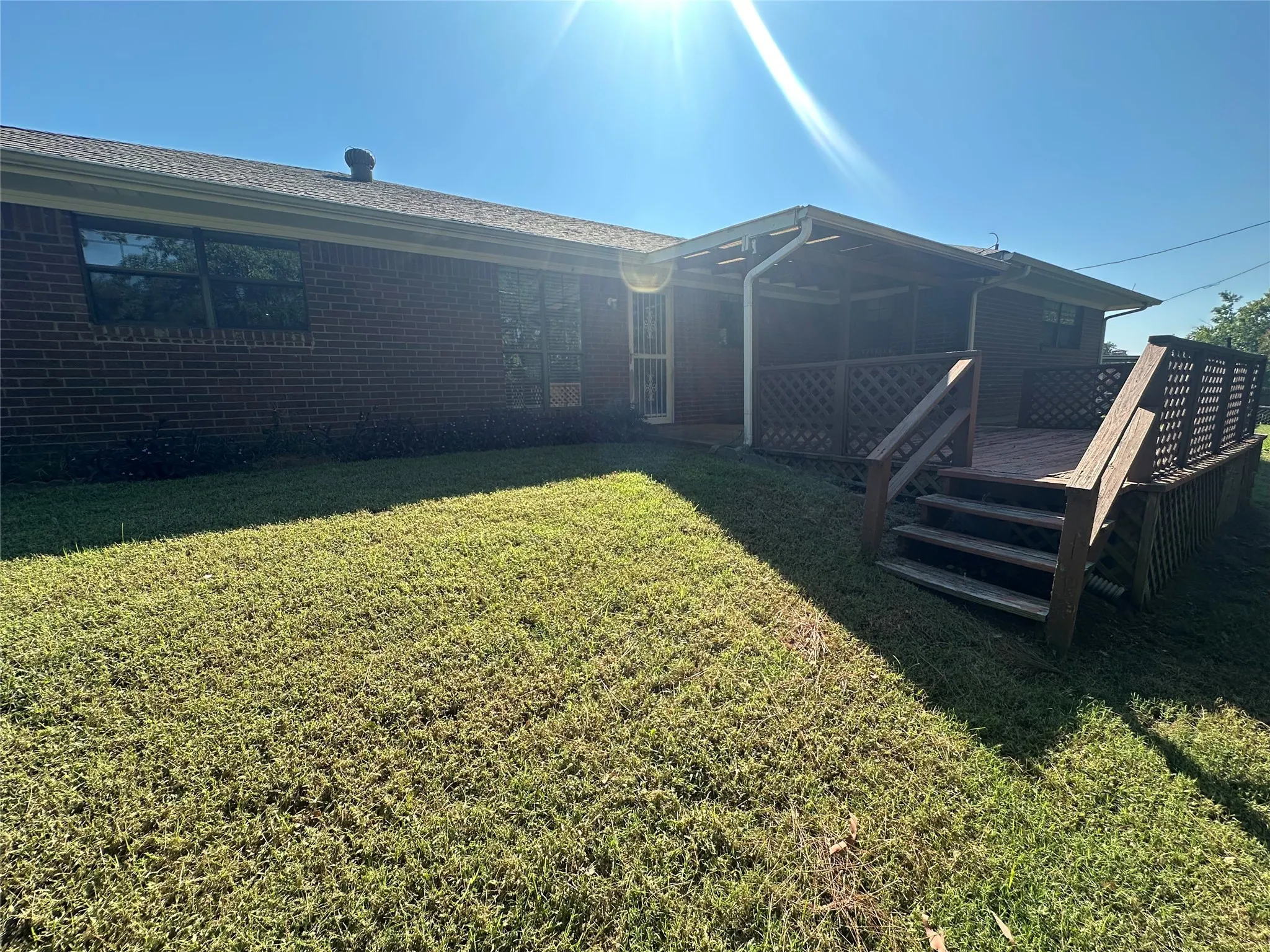 Back of house with a deck, a yard, and brick siding