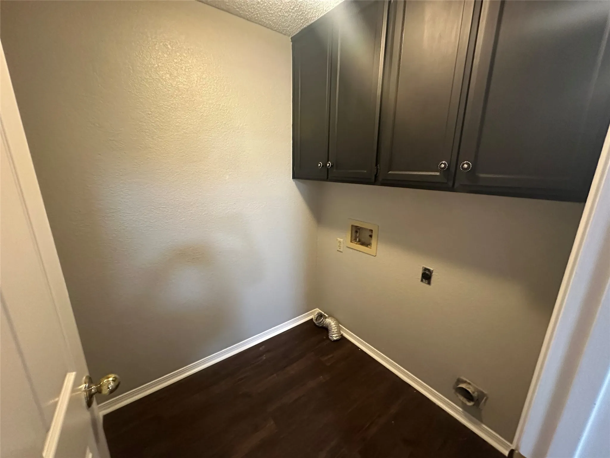 Laundry room with dark wood finished floors, washer hookup, cabinet space, electric dryer hookup, and a textured wall