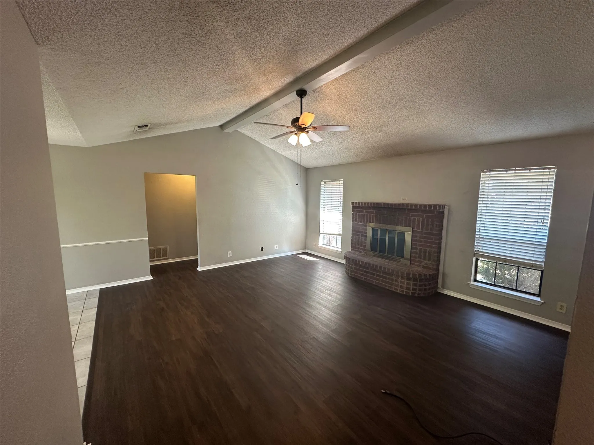 Unfurnished living room with a brick fireplace, wood finished floors, a textured ceiling, and a ceiling fan