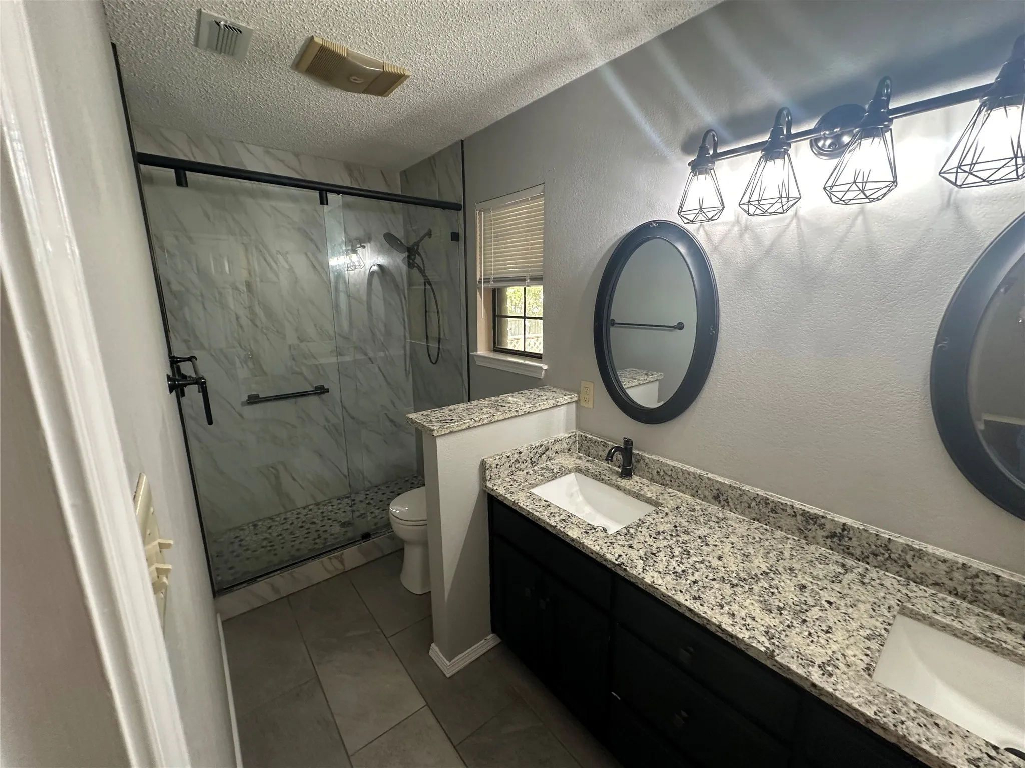 Bathroom featuring a marble finish shower, double vanity, a textured ceiling, dark tile patterned floors, and a textured wall