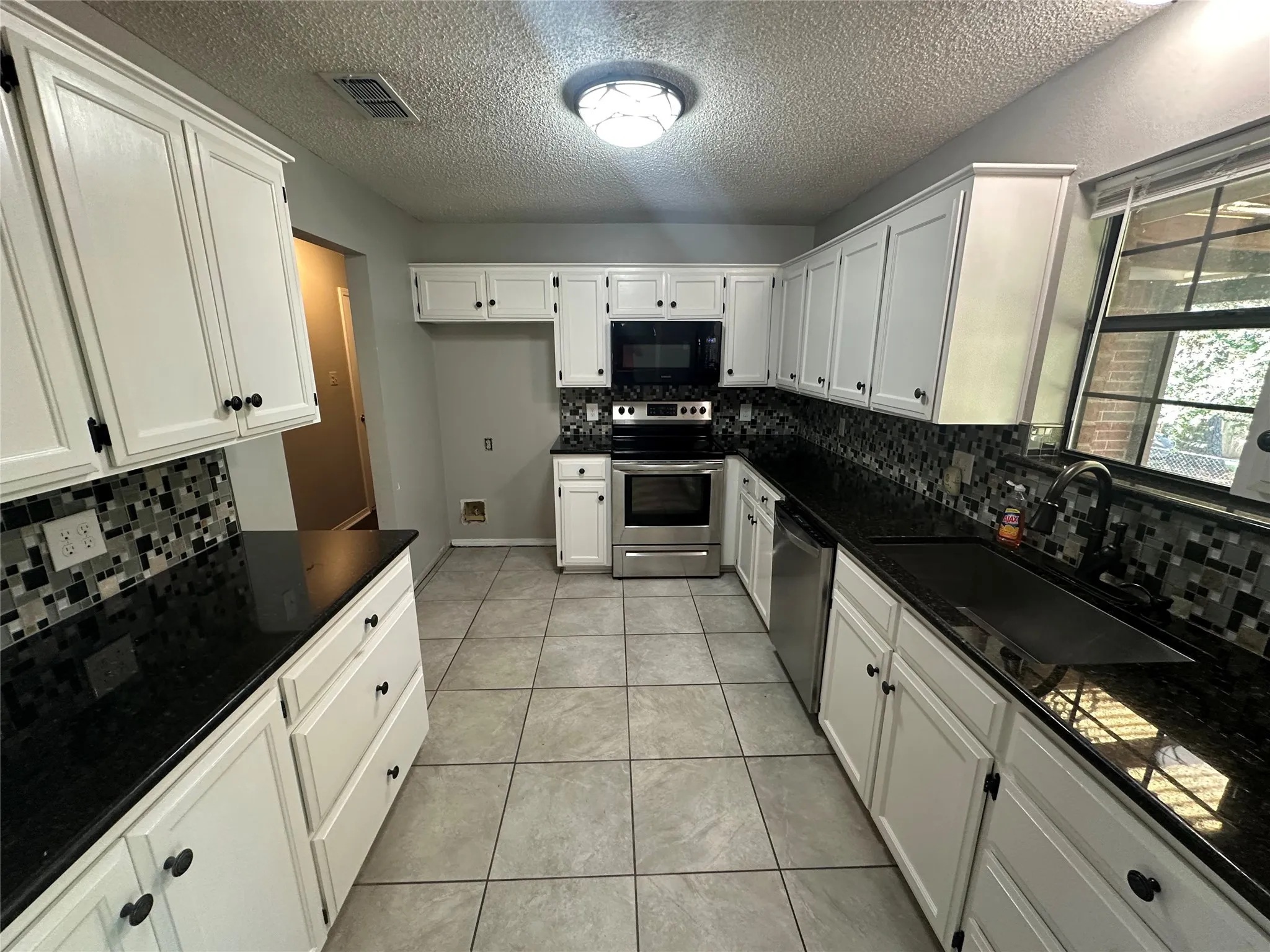 Kitchen with decorative backsplash, white cabinetry, appliances with stainless steel finishes, a textured ceiling, and light tile patterned flooring