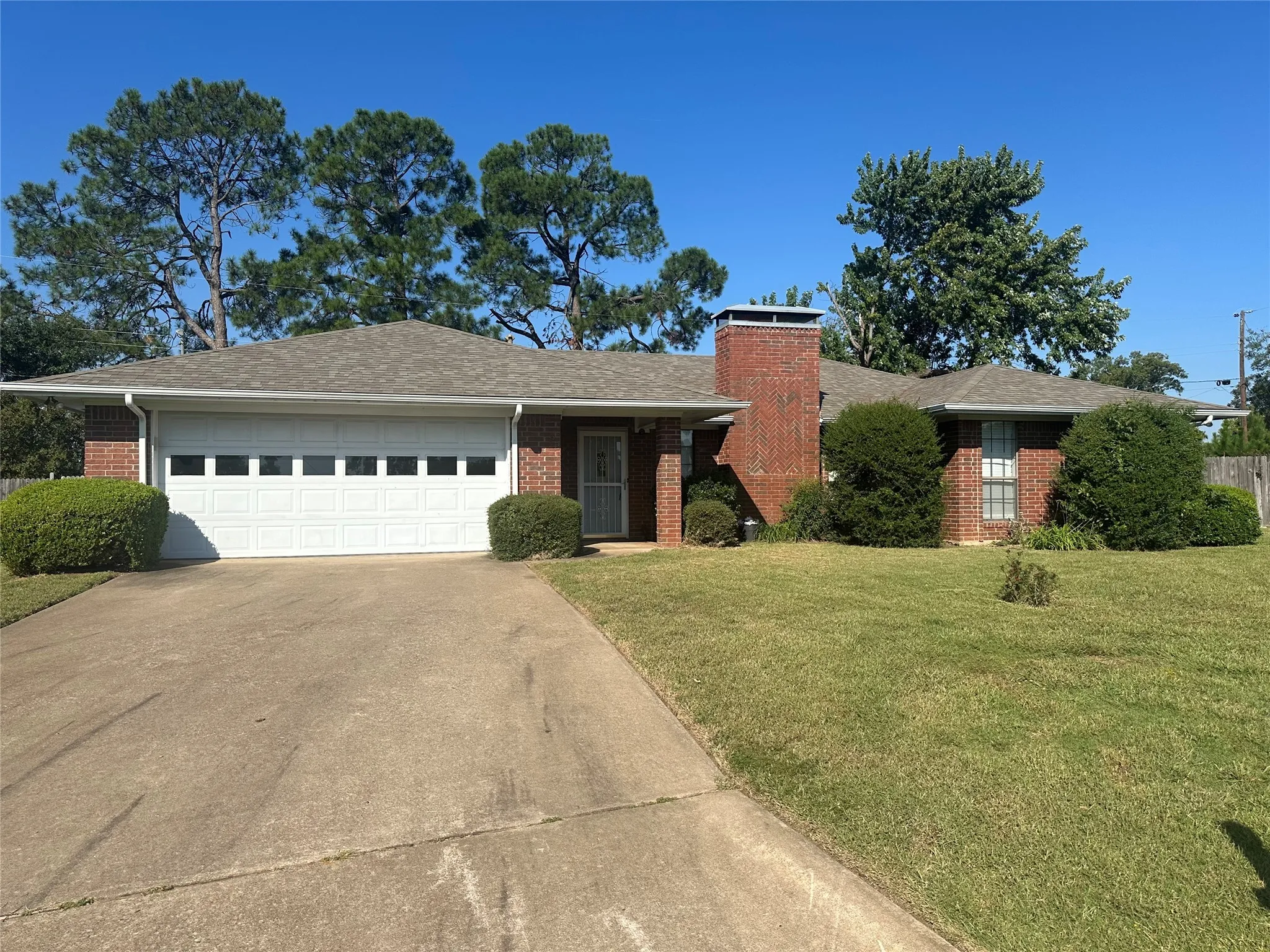 Ranch-style home featuring brick siding, a front lawn, concrete driveway, and roof with shingles