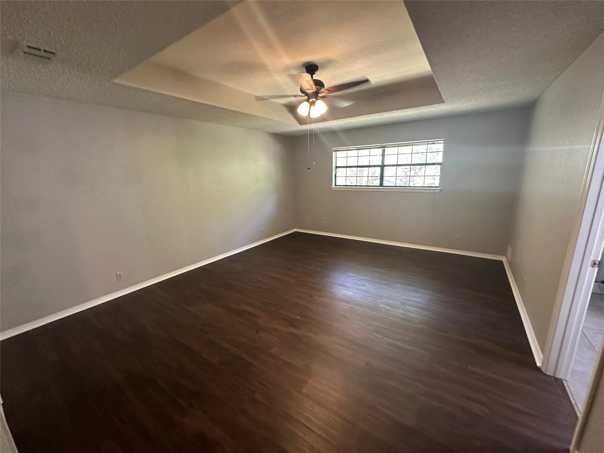 Empty room featuring a tray ceiling, dark wood-style floors, a textured ceiling, and a ceiling fan
