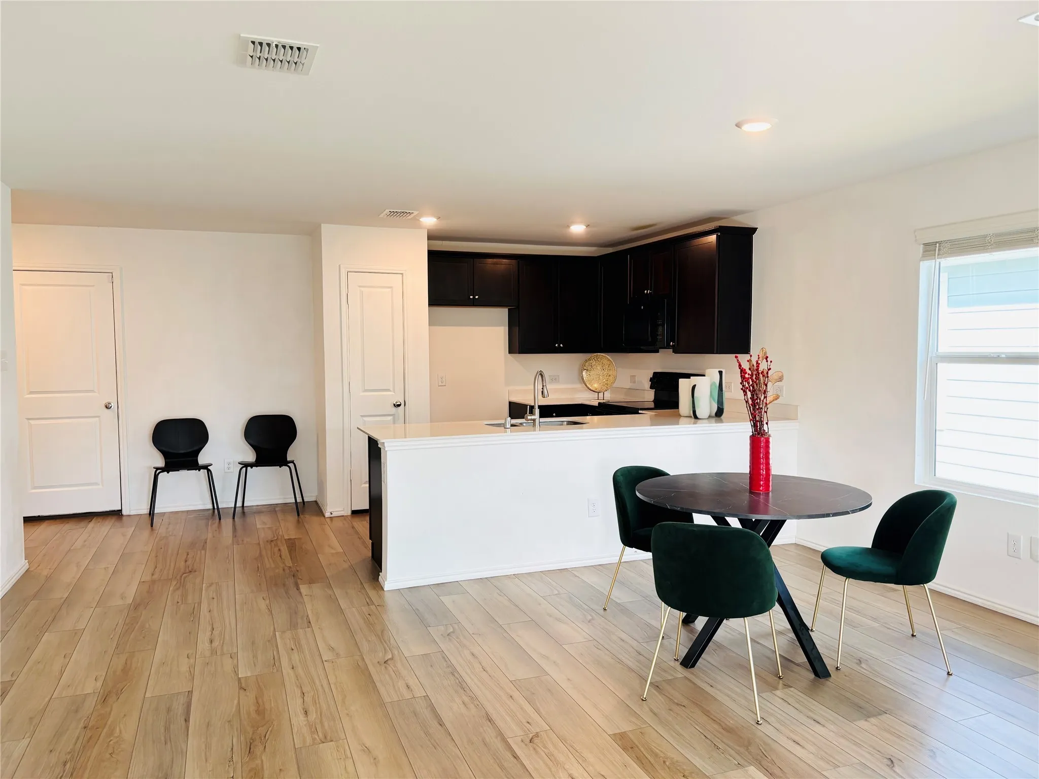 Kitchen with a peninsula, dark cabinetry, light wood-type flooring, light countertops, and black appliances