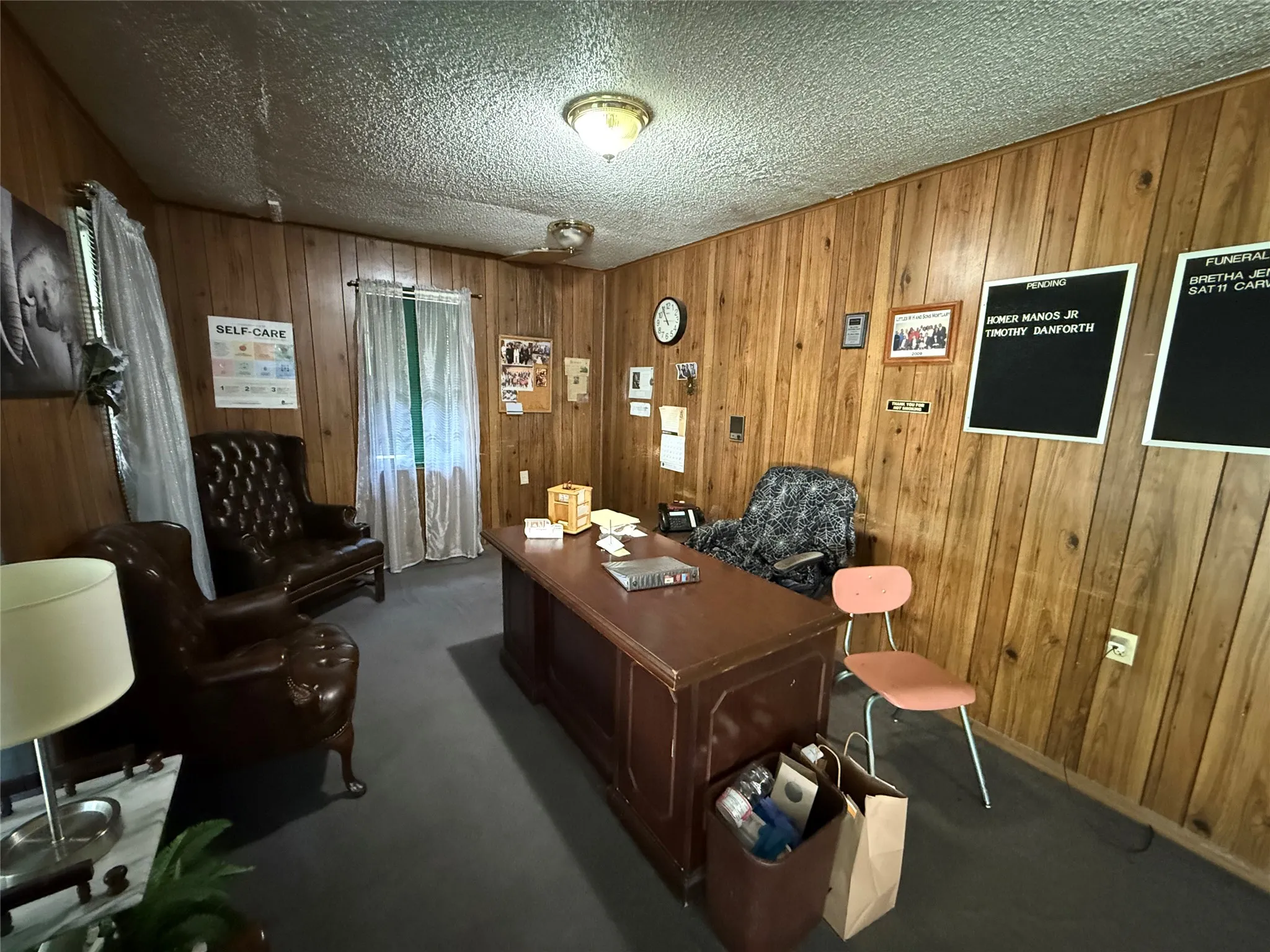 Home office featuring wooden walls, a textured ceiling, and dark carpet