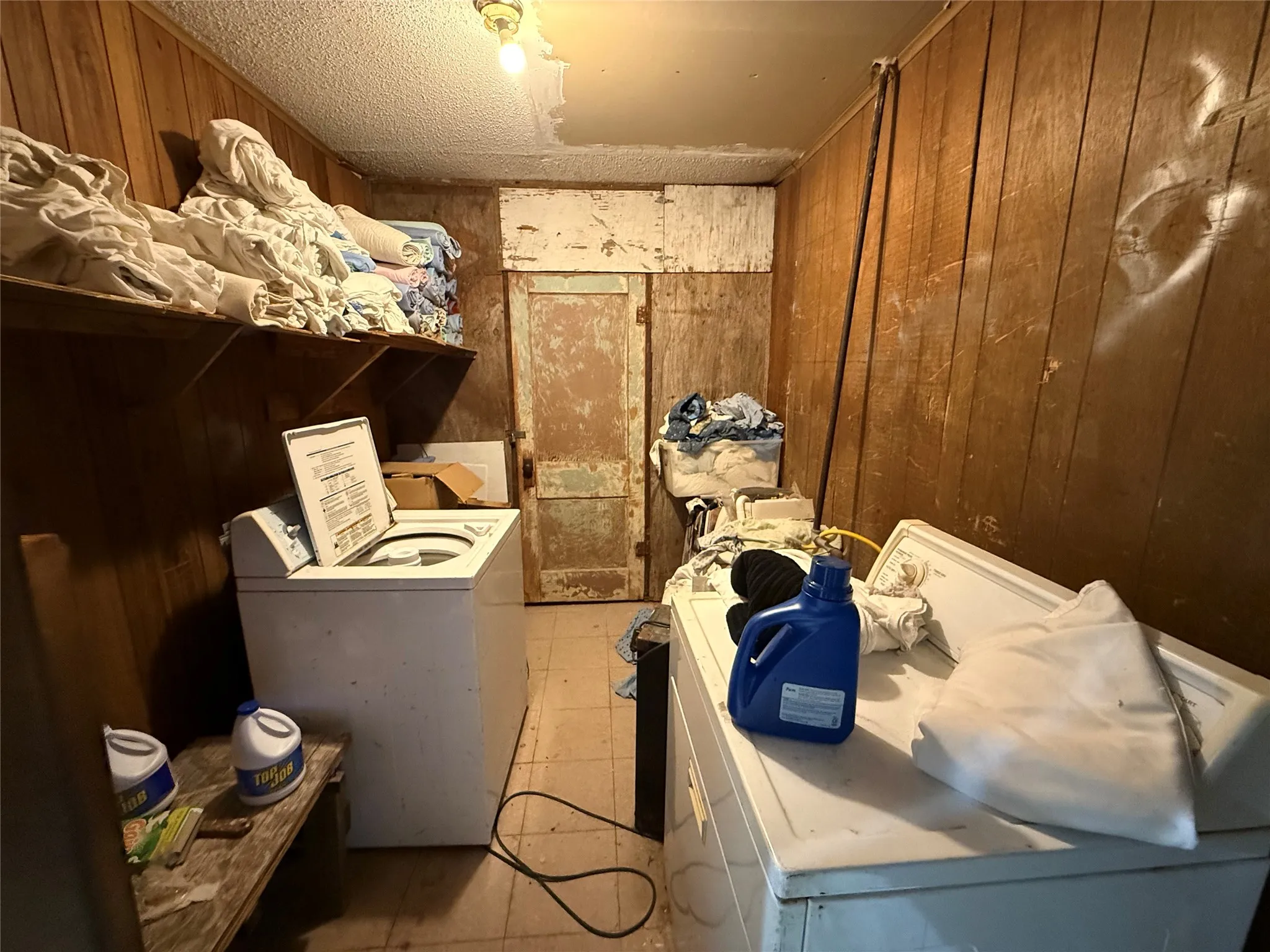 Laundry area with wood walls, washer and clothes dryer, and a textured ceiling