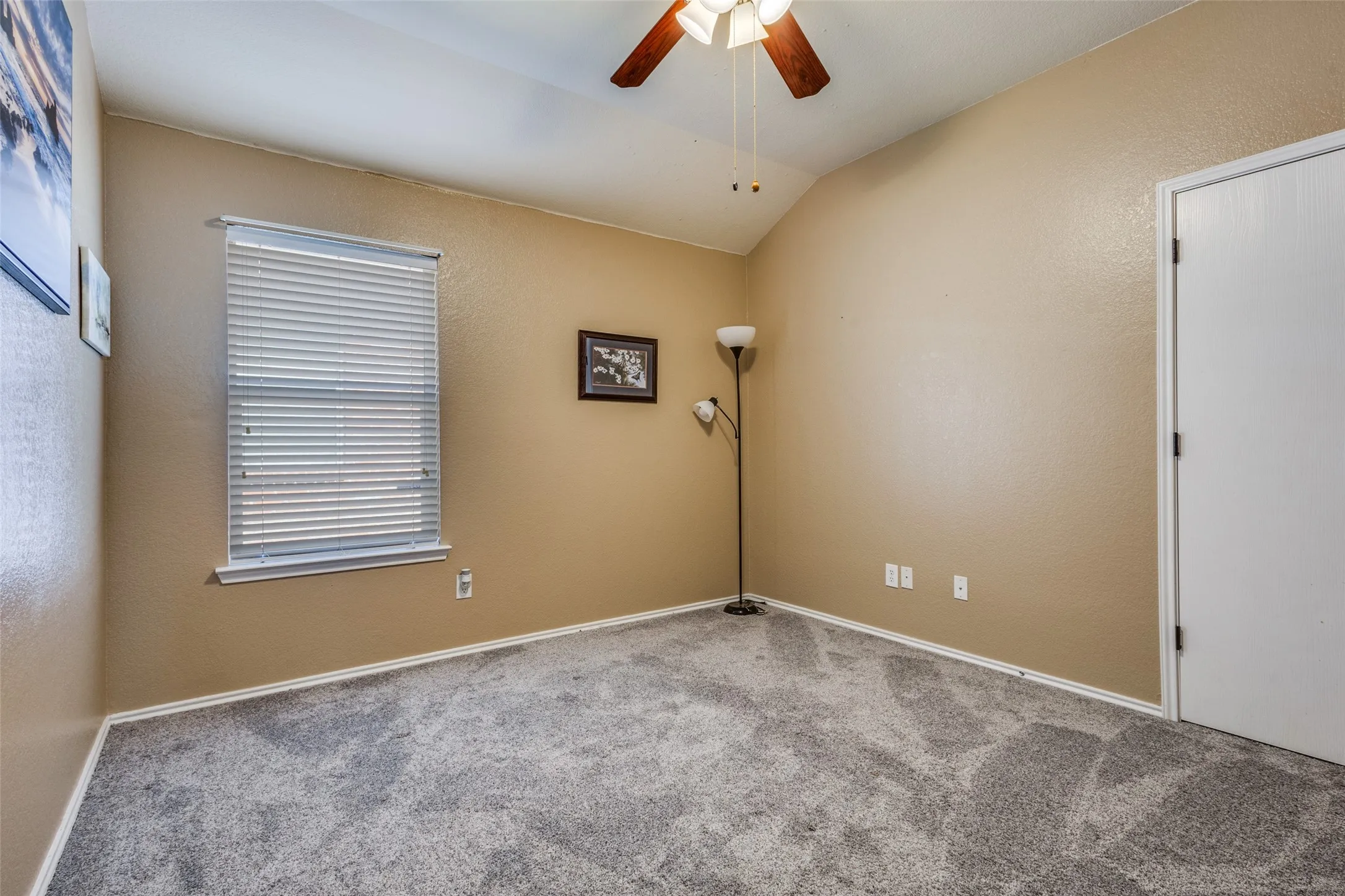Empty room with a textured wall, vaulted ceiling, a ceiling fan, and carpet flooring