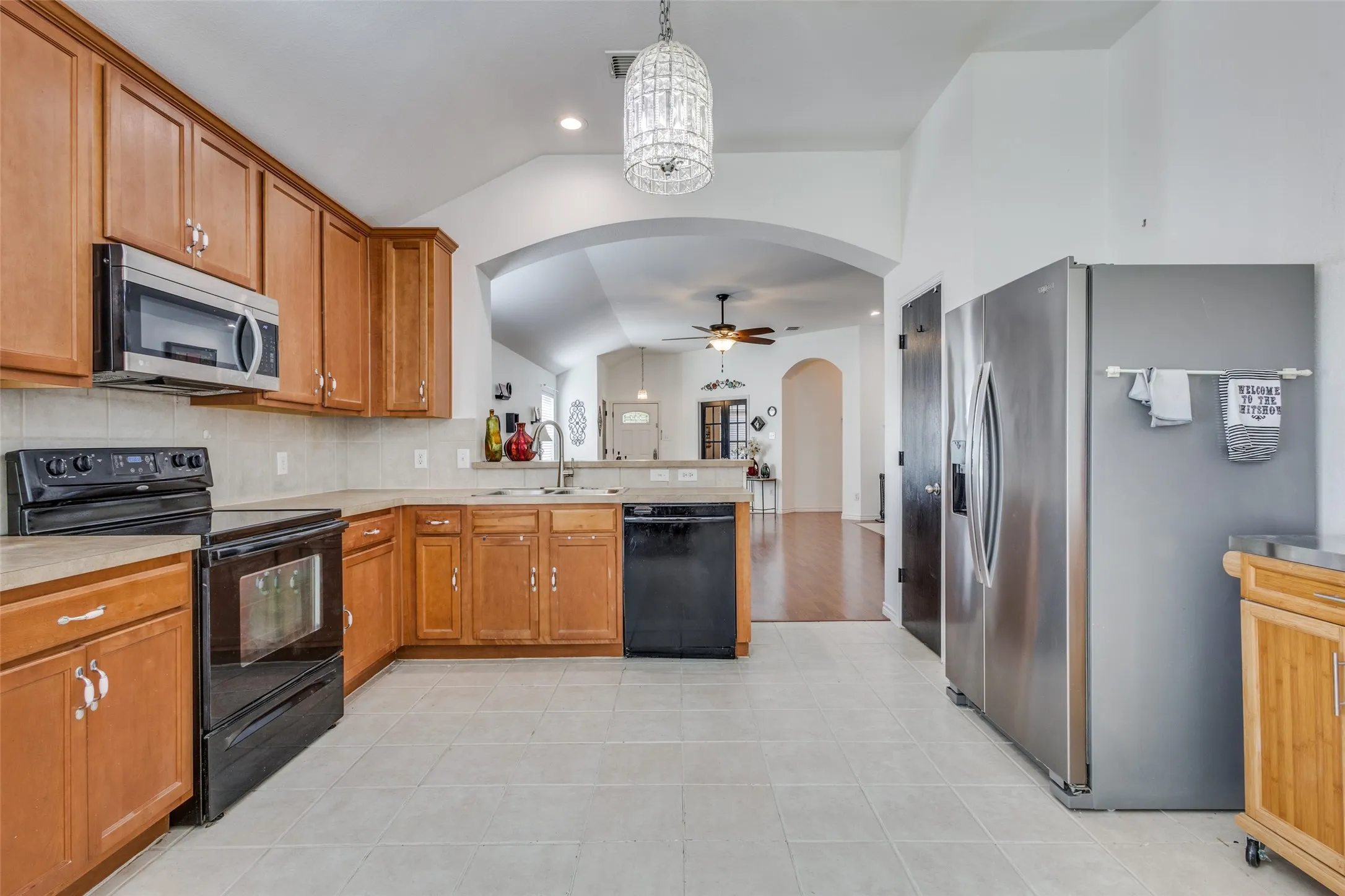 Kitchen with vaulted ceiling, black appliances, a chandelier, brown cabinetry, and backsplash