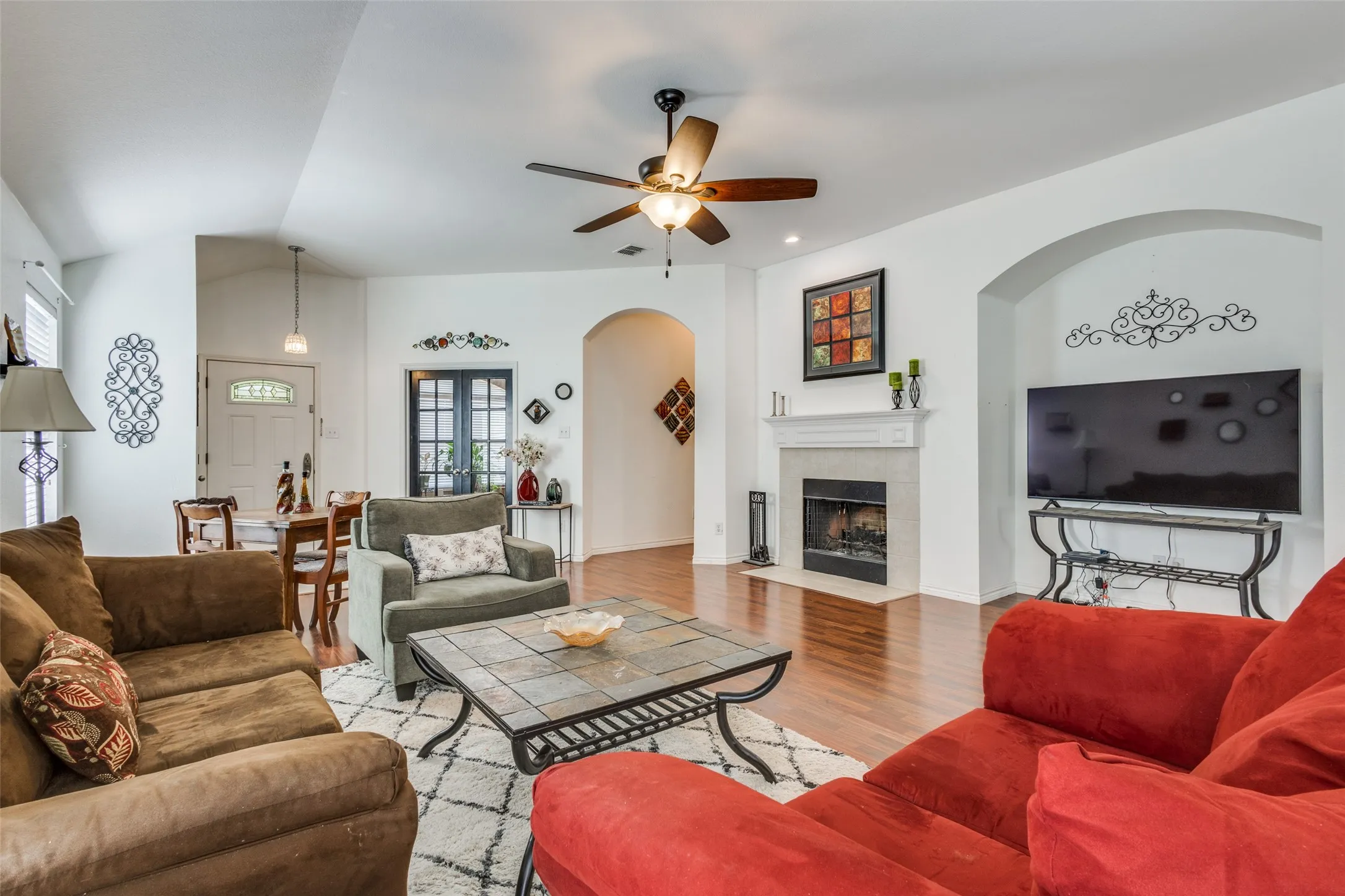 Living area with wood finished floors, arched walkways, a fireplace, a ceiling fan, and lofted ceiling