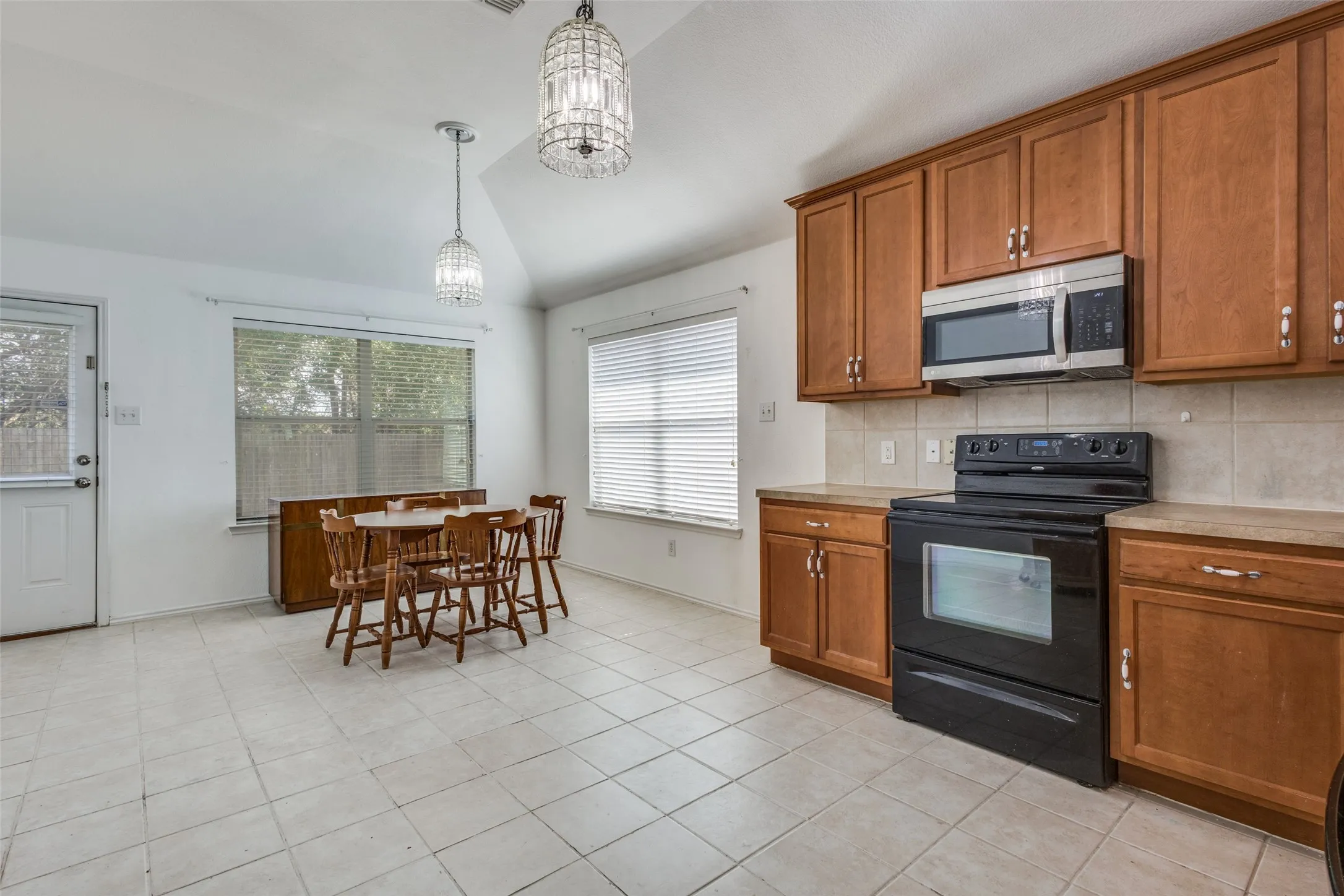 Kitchen with brown cabinetry, black electric range, stainless steel microwave, and vaulted ceiling