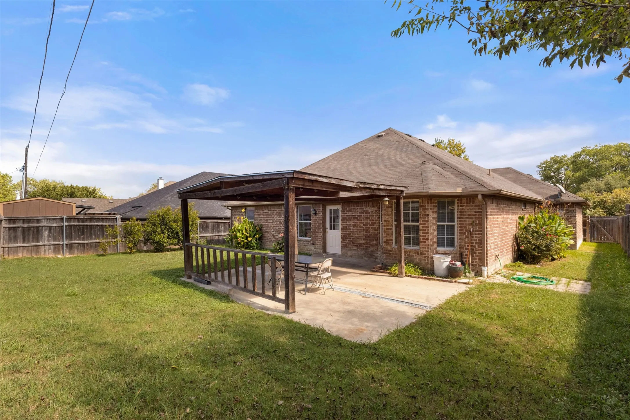Rear view of property with a fenced backyard, brick siding, a patio area, and roof with shingles