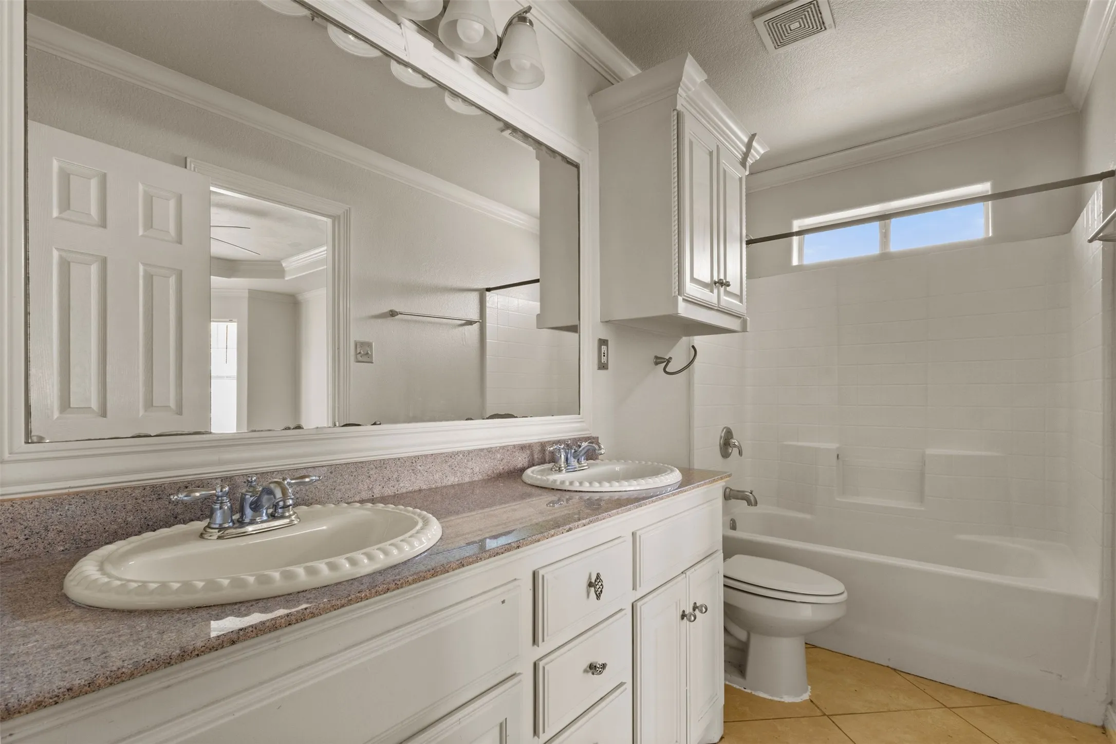 Full bathroom with ornamental molding, washtub / shower combination, light tile patterned floors, double vanity, and a textured ceiling